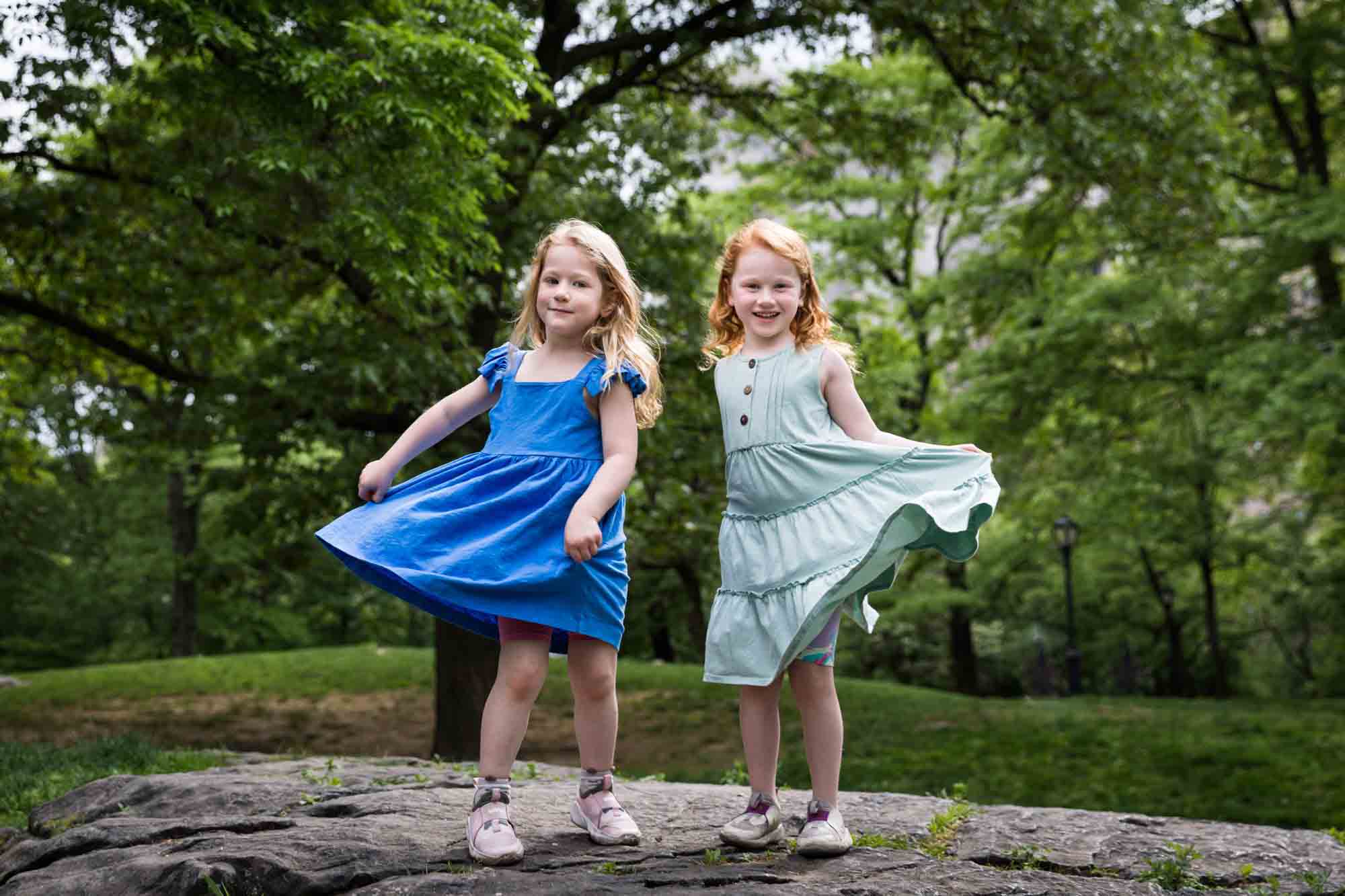 Two little girls wearing blue dresses dancing on rock during a Central Park family portrait session