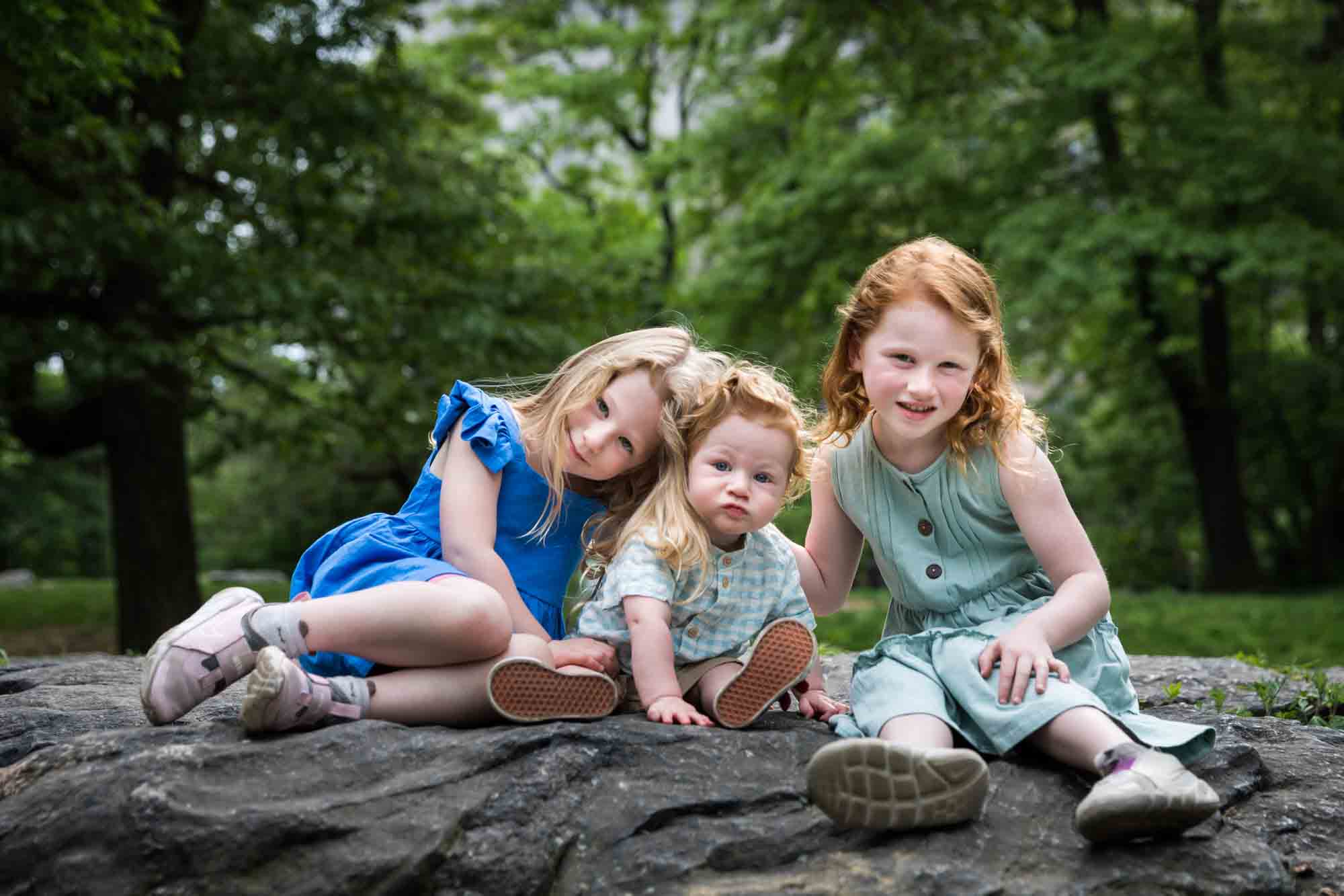 Two little girls with red-haired baby boy sitting on rock during a Central Park family portrait session