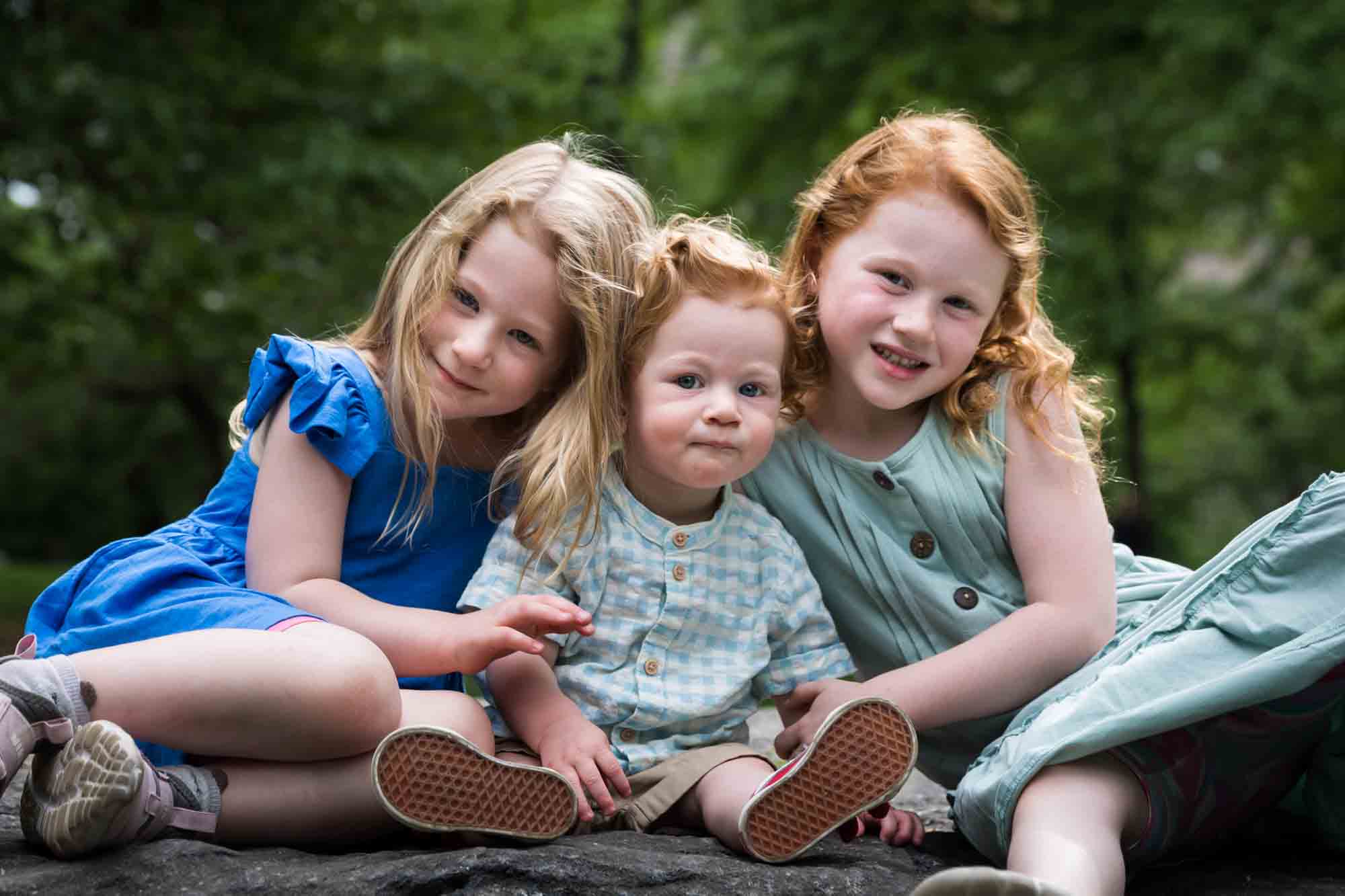 Two little girls with red-haired baby boy sitting on rock during a Central Park family portrait session