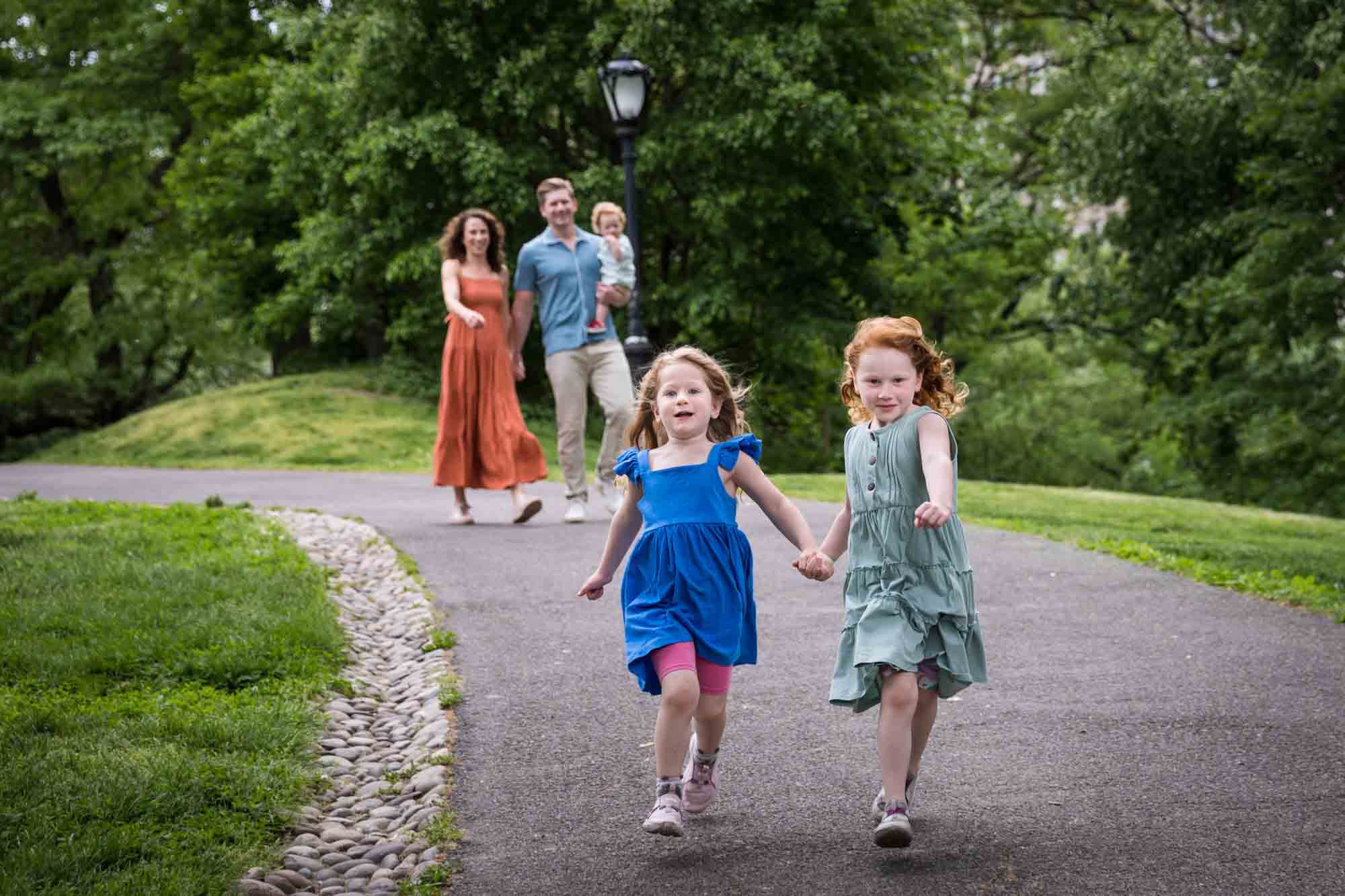 Two little girls holding hands wearing blue dresses running down pathway during a Central Park family portrait session