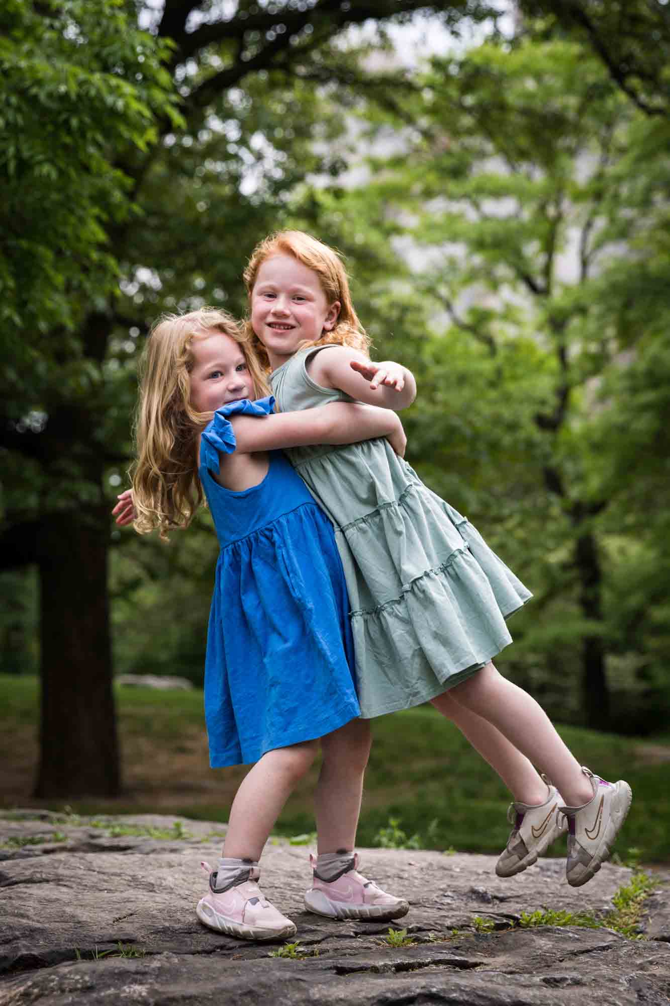 Two little girls wearing blue dresses hugging on rock during a Central Park family portrait session