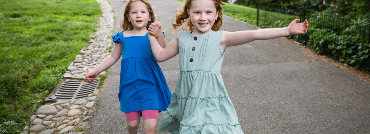 Two little girls holding hands wearing blue dresses running down pathway during a Central Park family portrait session