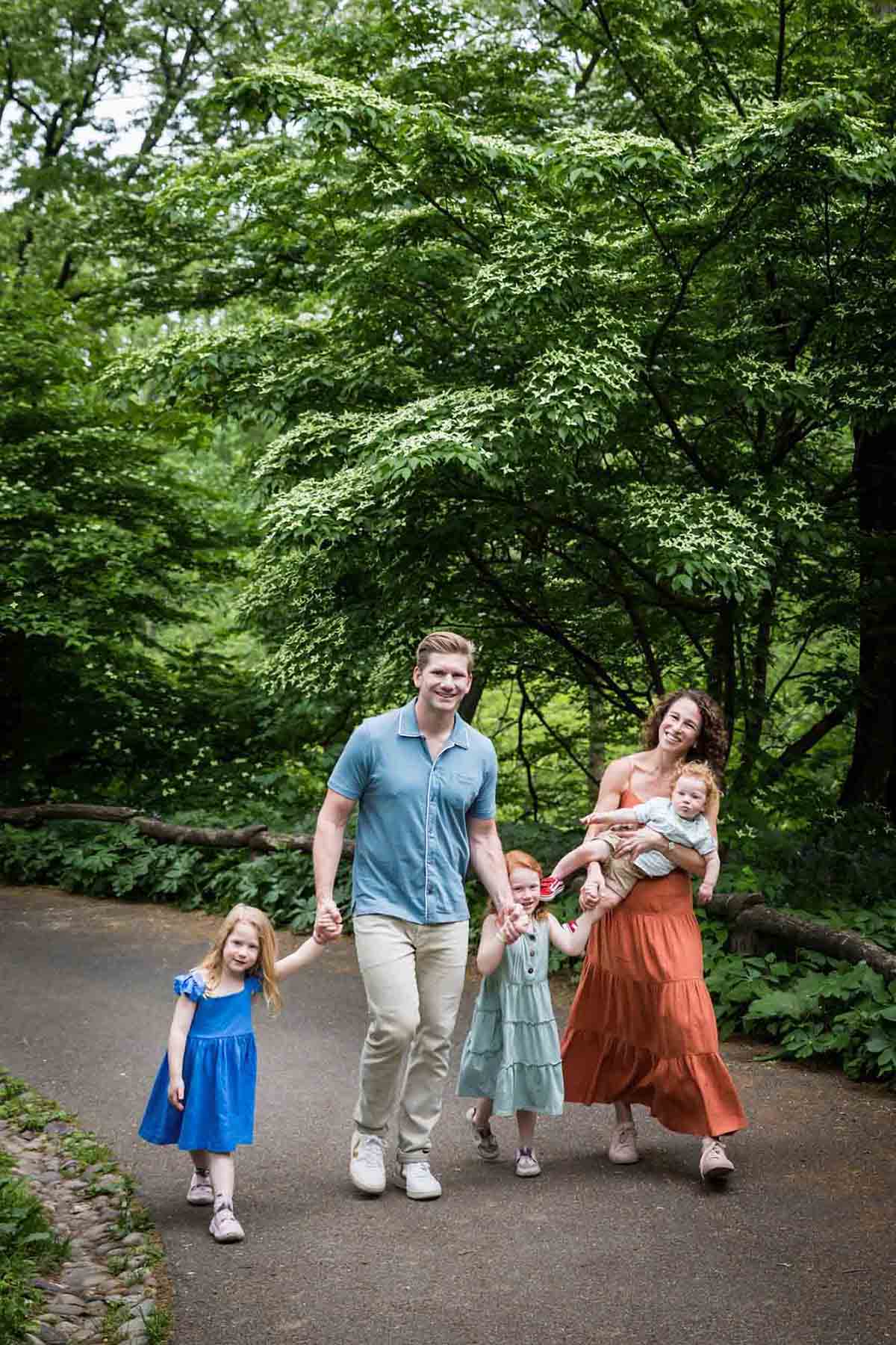 Mother and father with three kids walking up pathway in front of trees during a Central Park family portrait session