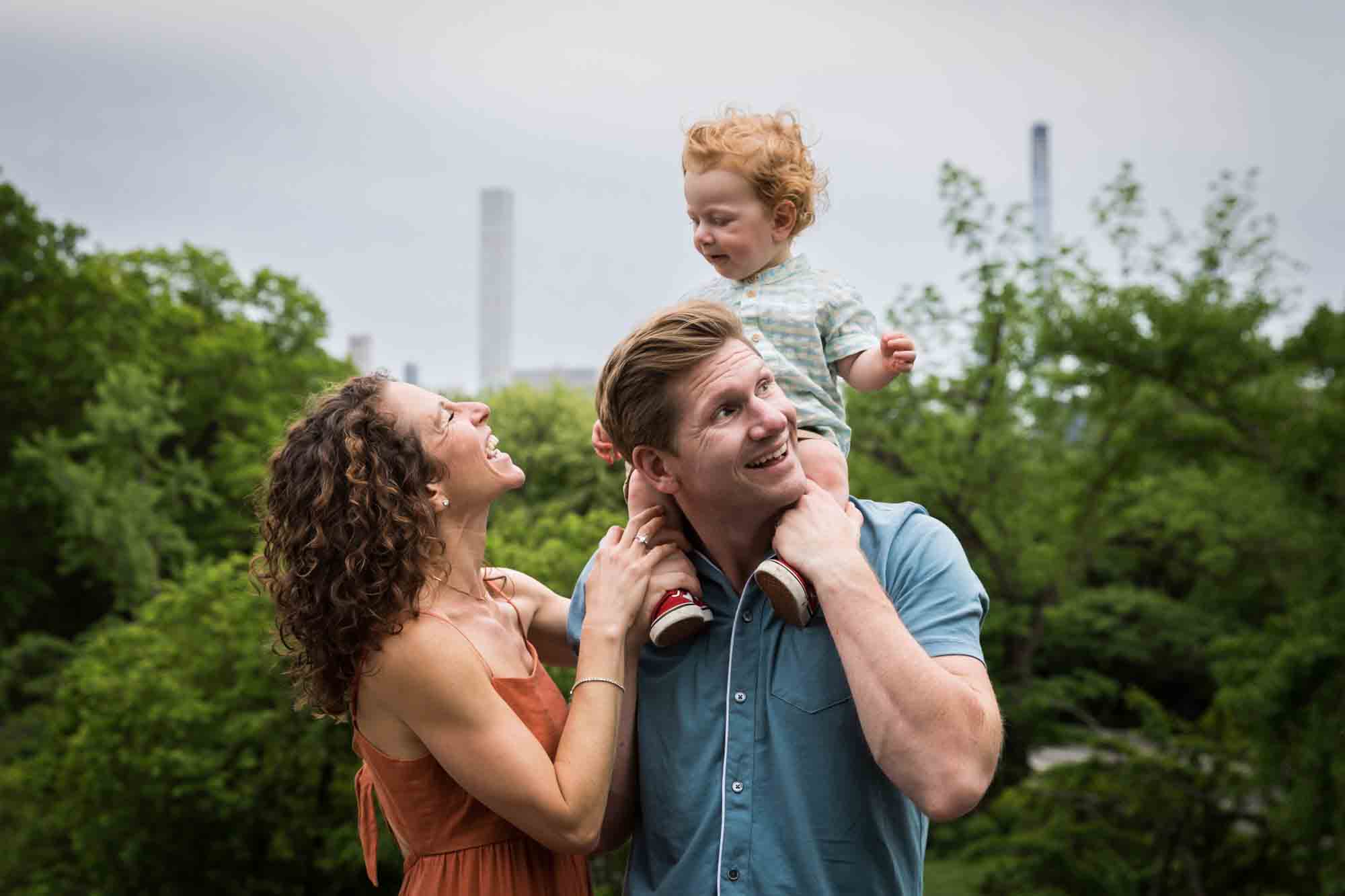 Mother and father looking back at red-haired baby boy held on father's shoulders during a Central Park family portrait session