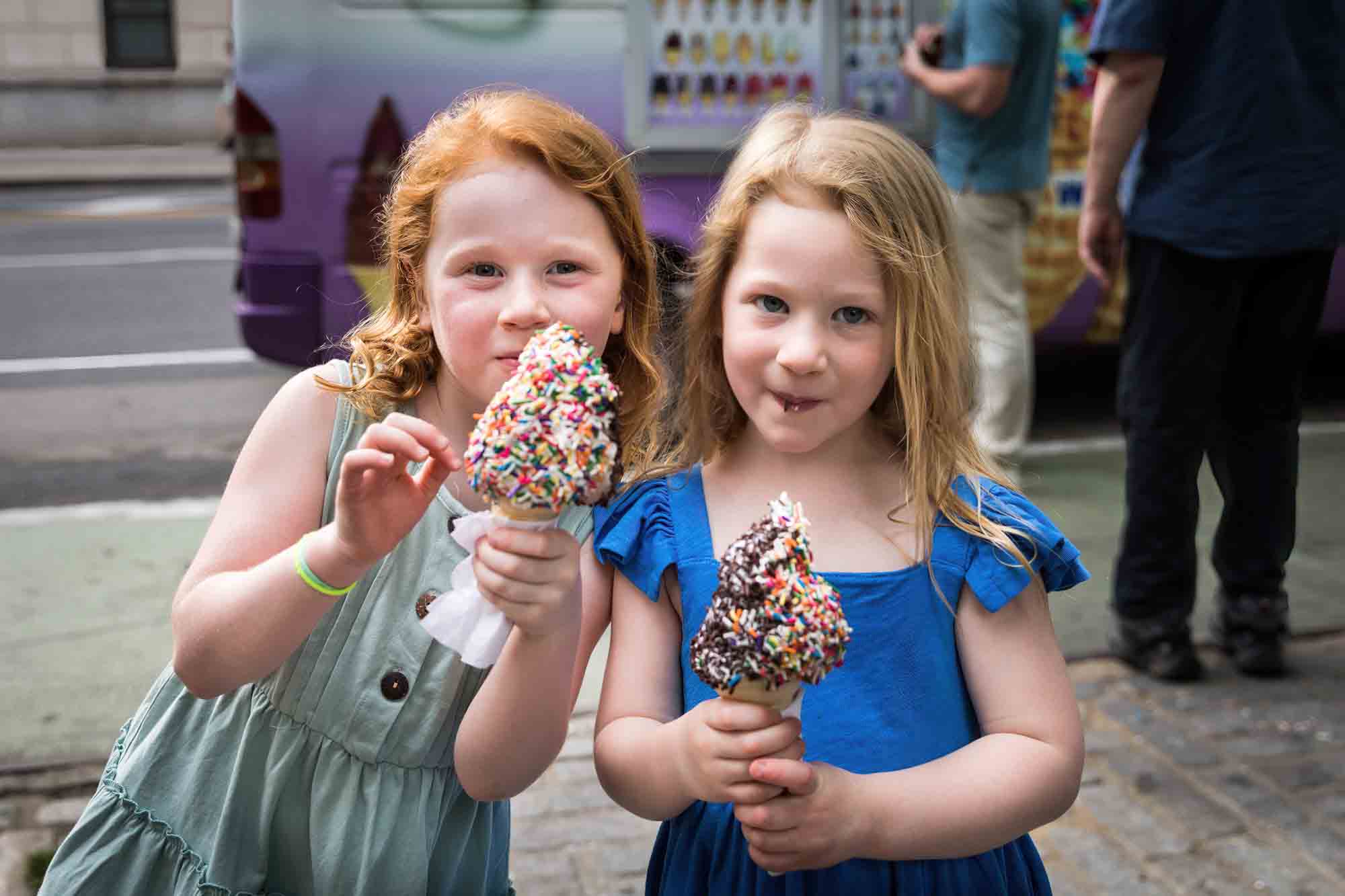 Two little girls holding ice cream cones covered in colorful sprinkles