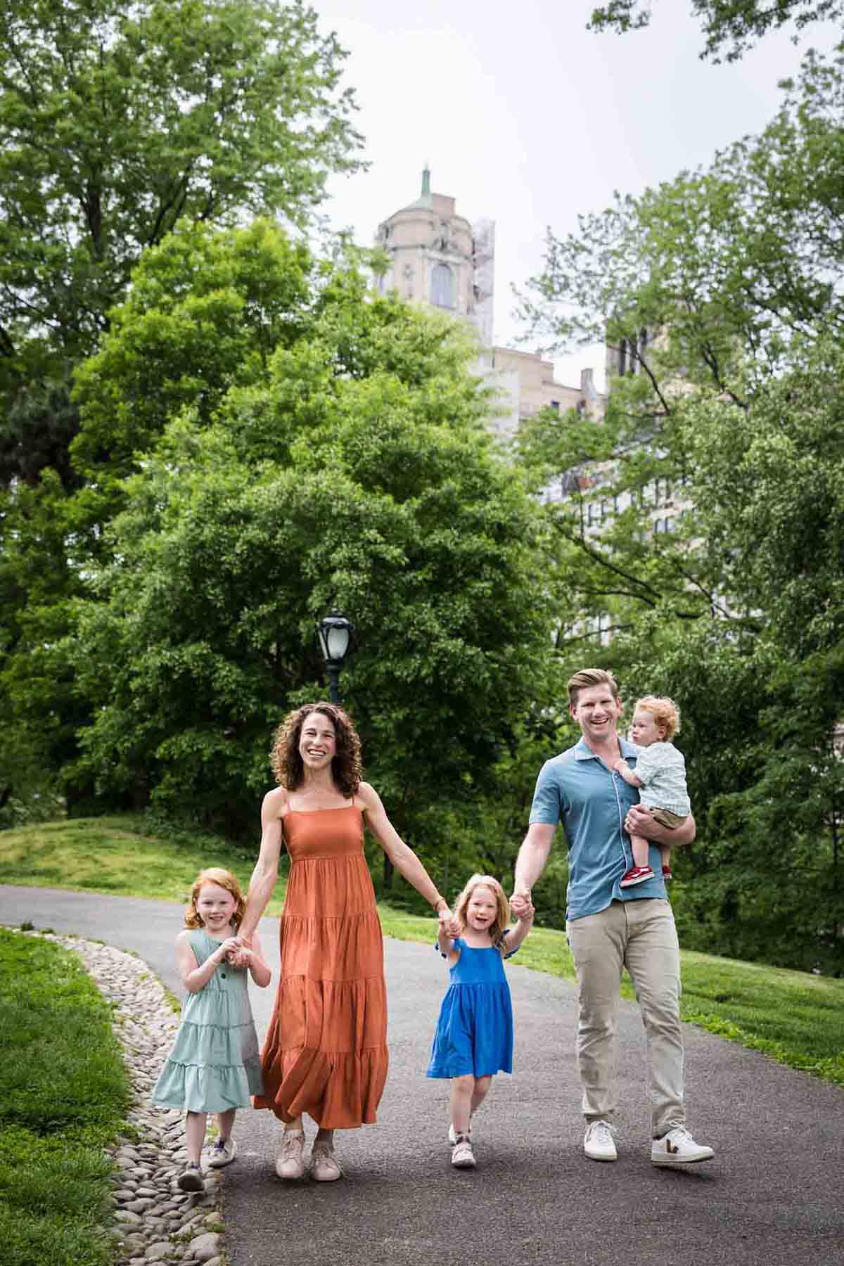 Mother and father with three kids walking up pathway in front of trees during a Central Park family portrait session