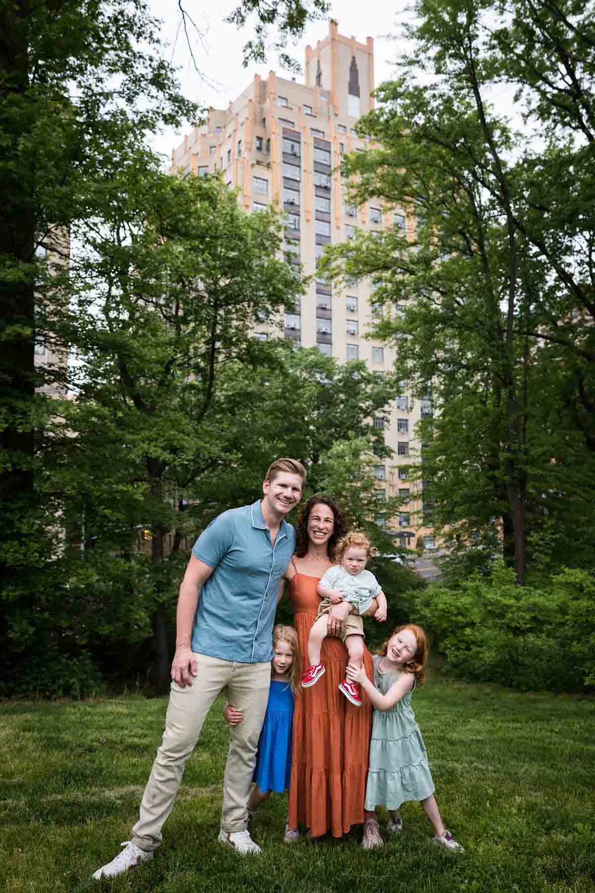Family with three children standing in grass in front of building during a Central Park family portrait session