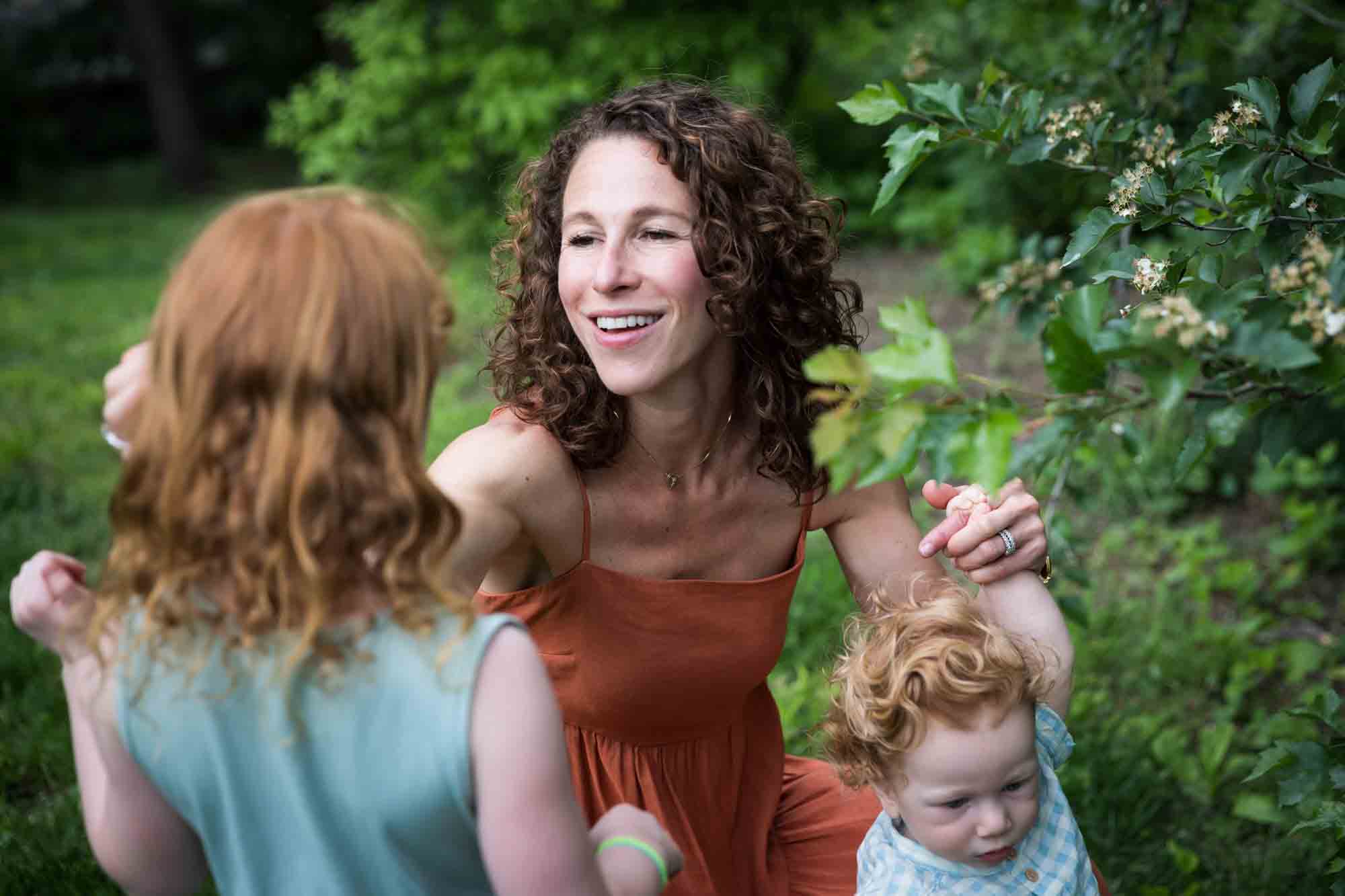 Mother holding hand of little boy and reaching out to child while sitting in grass