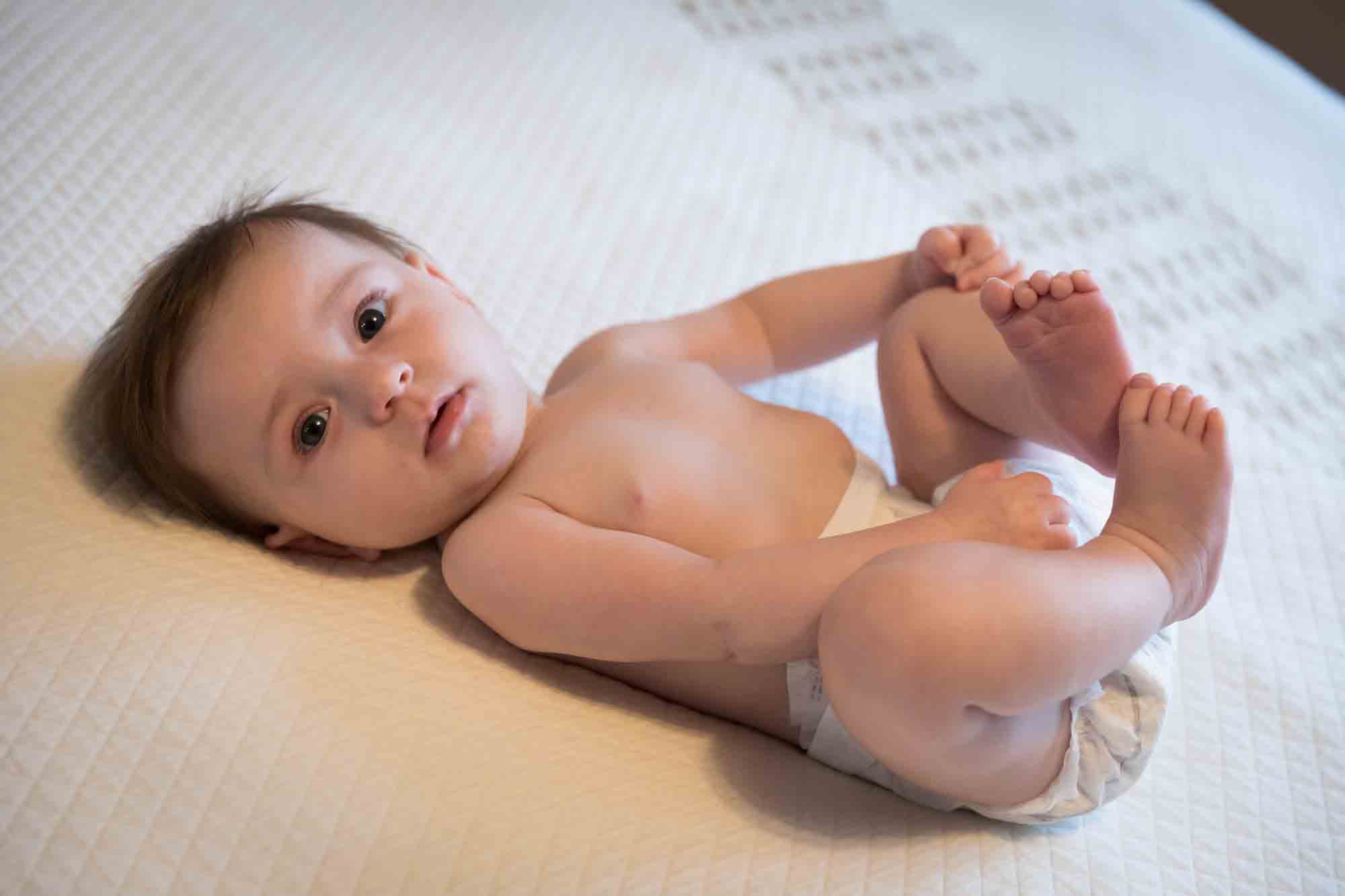 Naked baby wearing diaper on white bedspread