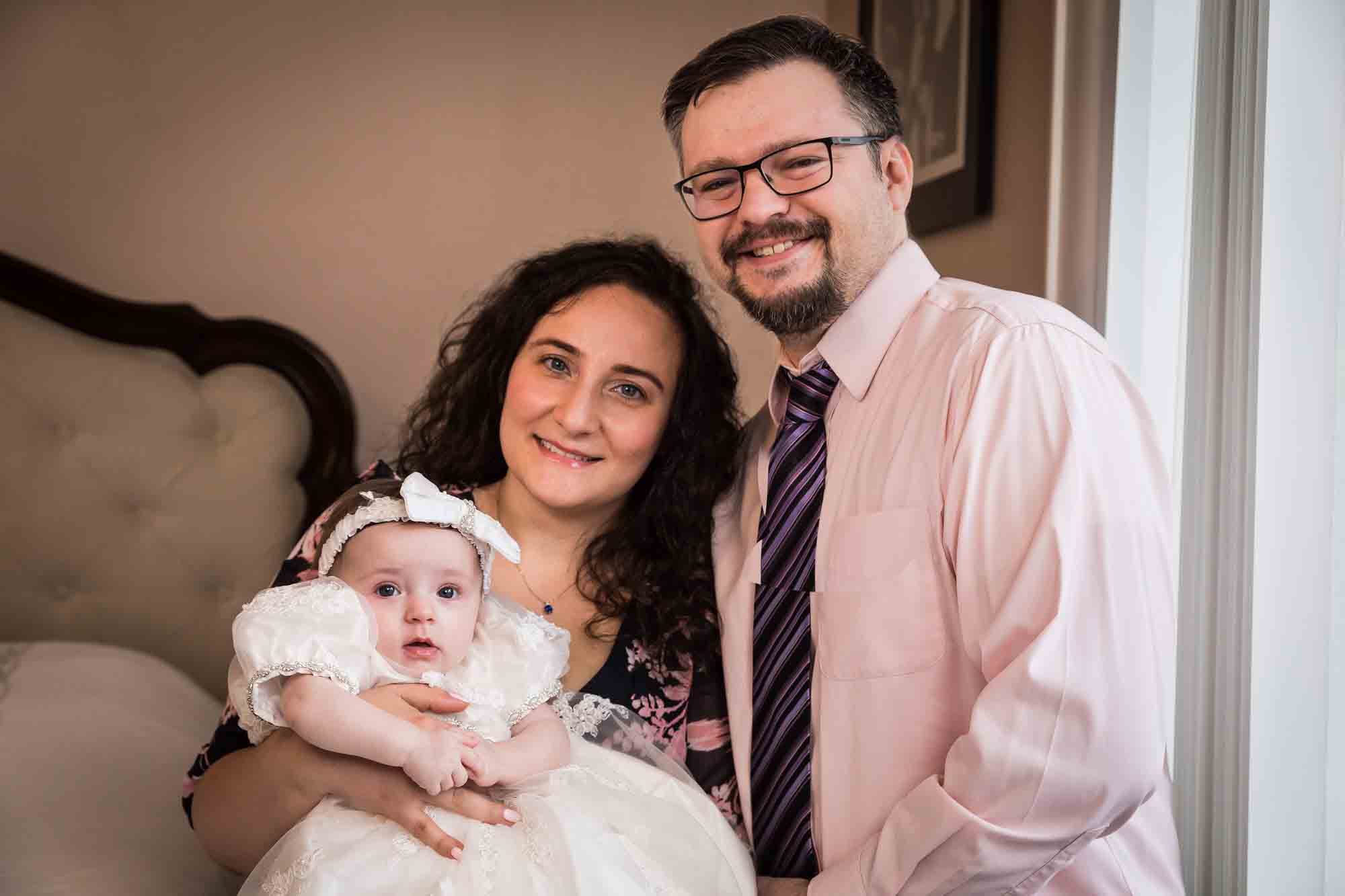 Mother and father holding baby girl wearing white baptism dress and hair bow