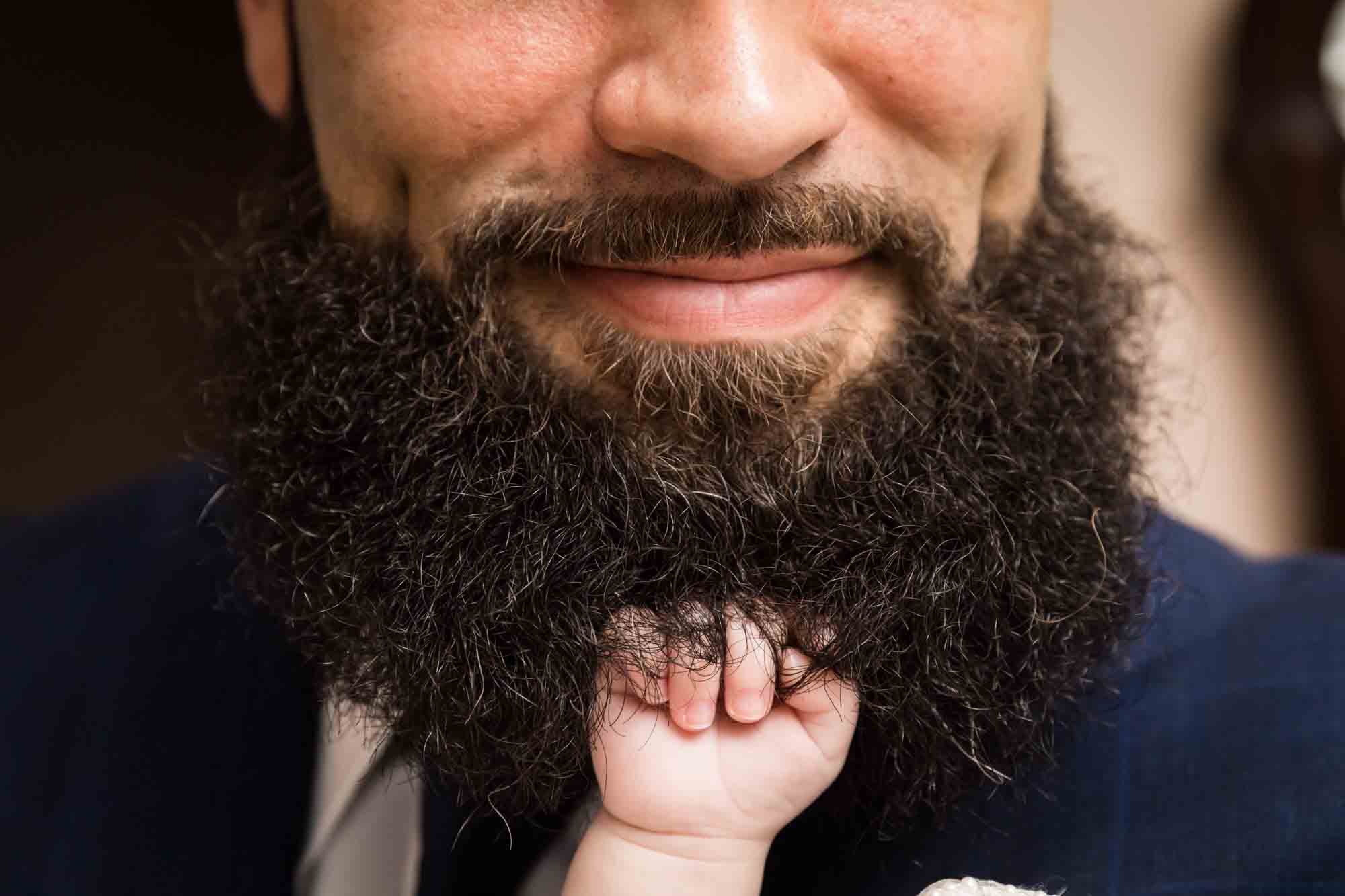 Close up of tiny baby hand holding man's bush beard