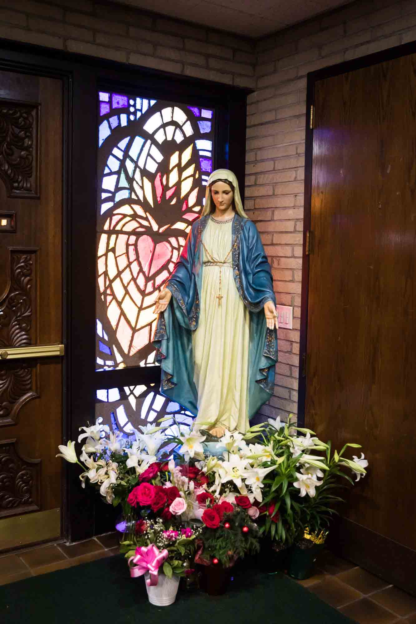 Statue of Virgin Mary in front of stained glass window with colorful flowers