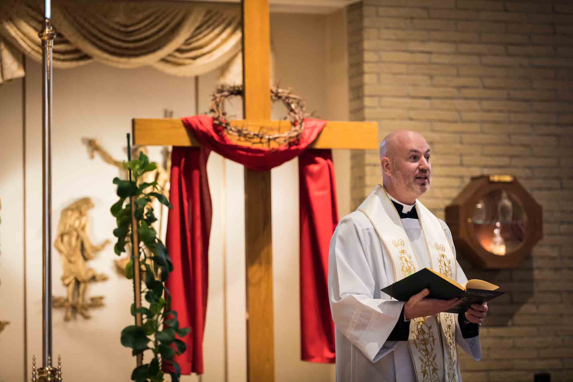 Maspeth baptism photos of priest speaking in front of wooden cross with red fabric