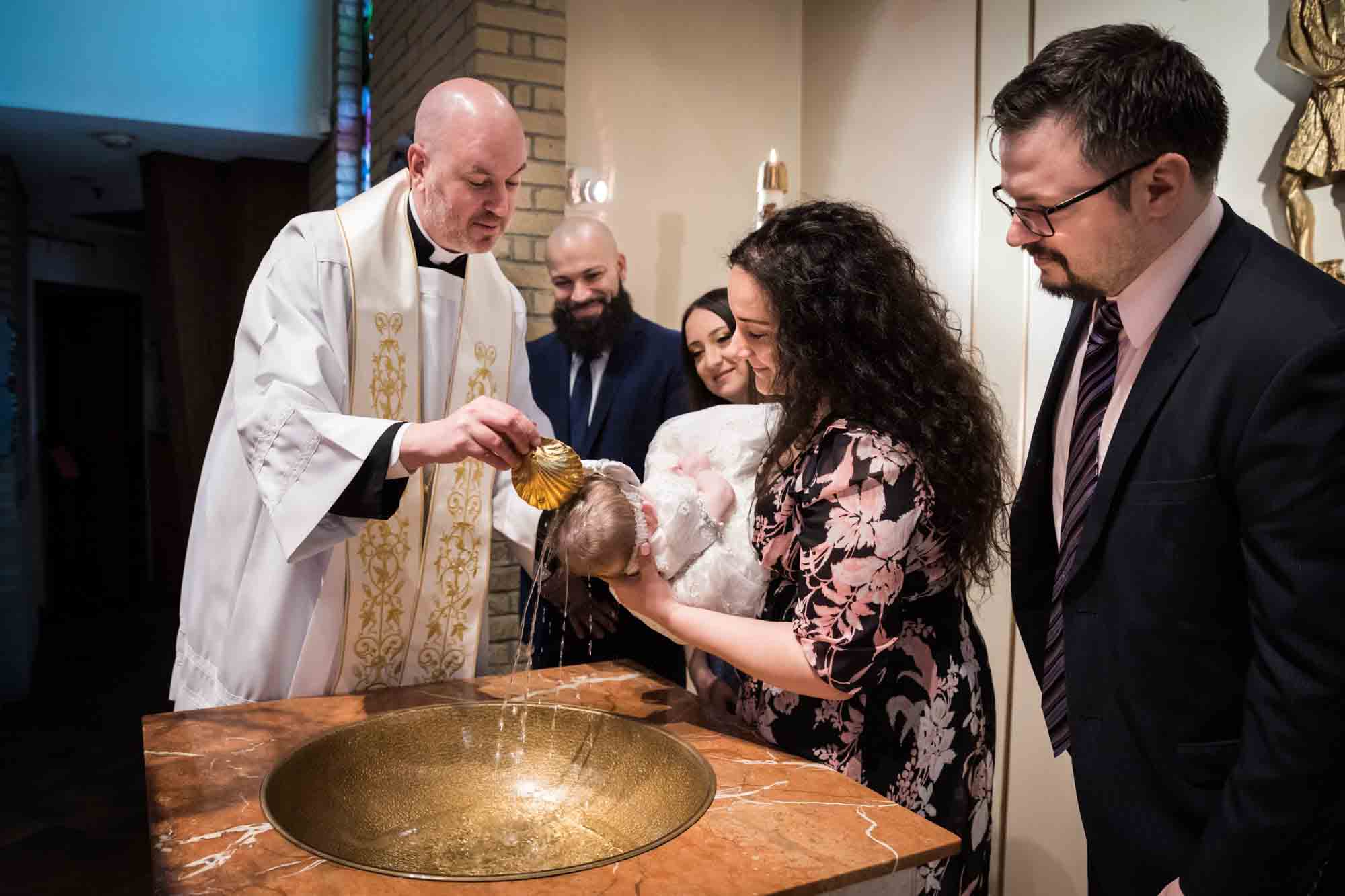 Maspeth baptism photos of priest pouring water on baby's head with family watching