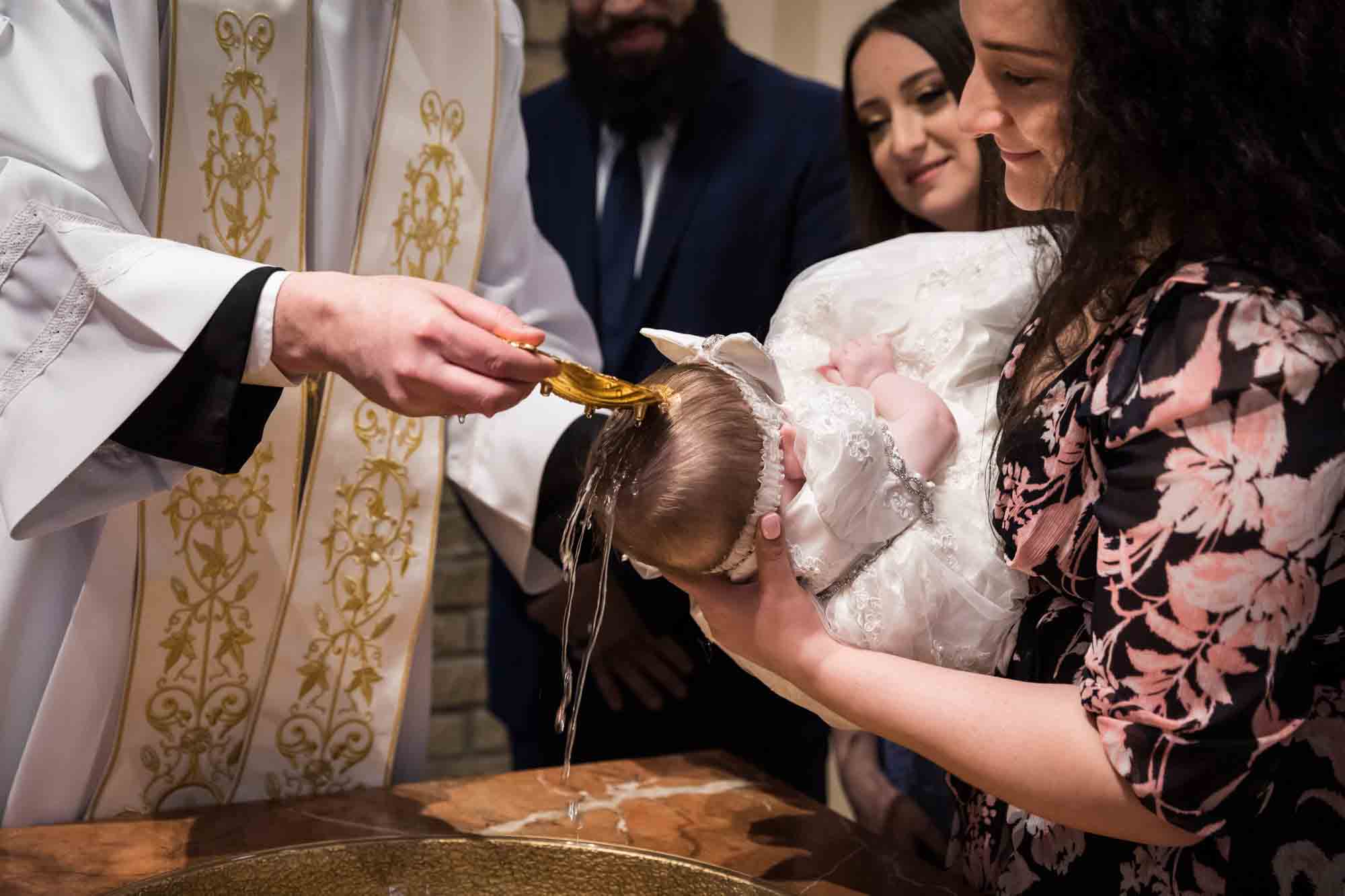 Maspeth baptism photos of priest's hand pouring water on baby's head with family watching