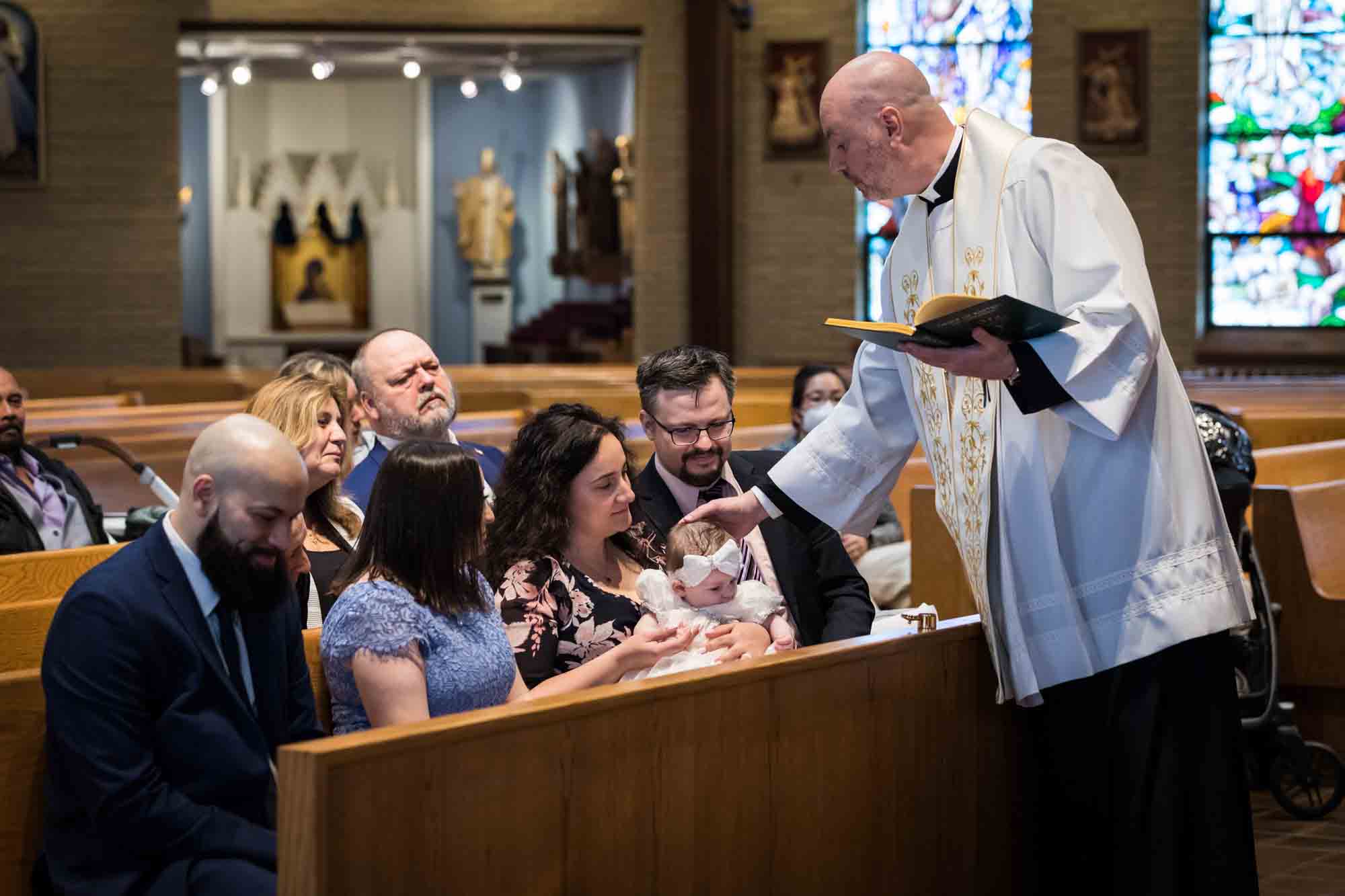 Maspeth baptism photos of priest anointing baby's head with oil in front of family