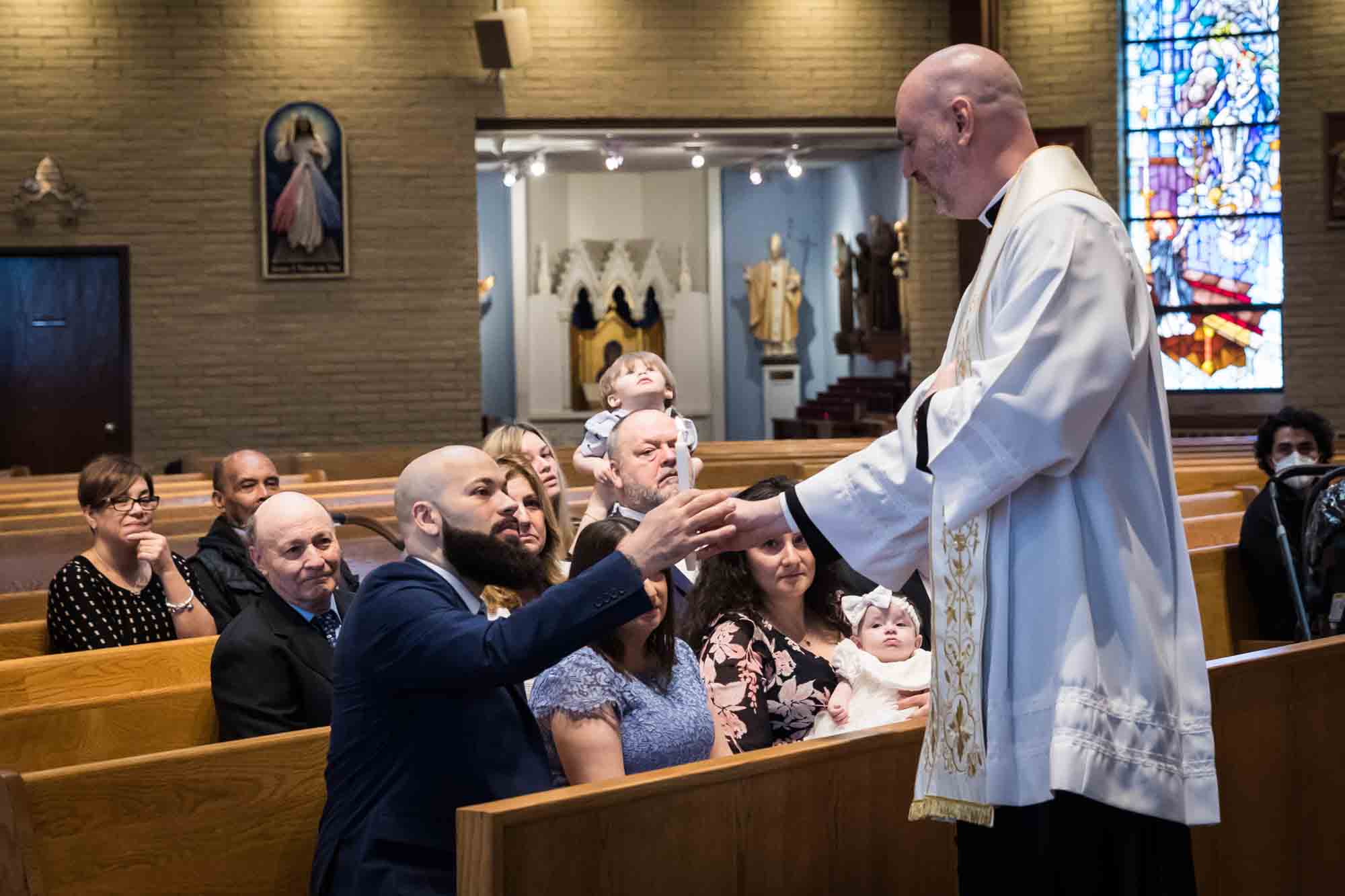 Maspeth baptism photos of priest giving lit candle to godfather in pew