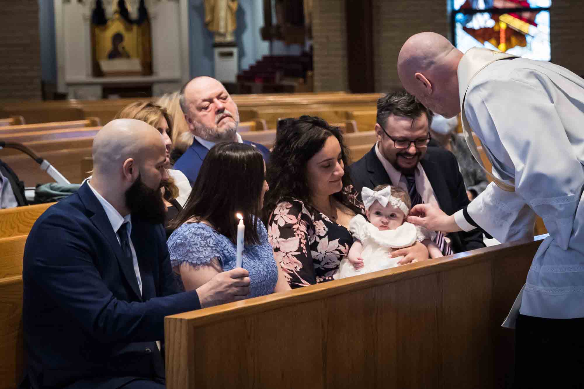 Maspeth baptism photos of priest anointing baby's head with oil in front of family
