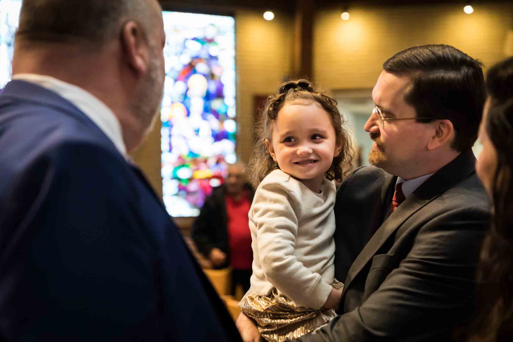 Maspeth baptism photos of father holding smiling little girl in front of stained glass window