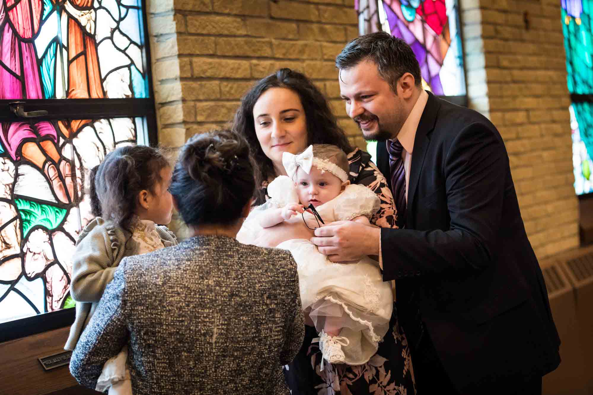 Maspeth baptism photos of parents showing baby to family members in front of stained glass windows