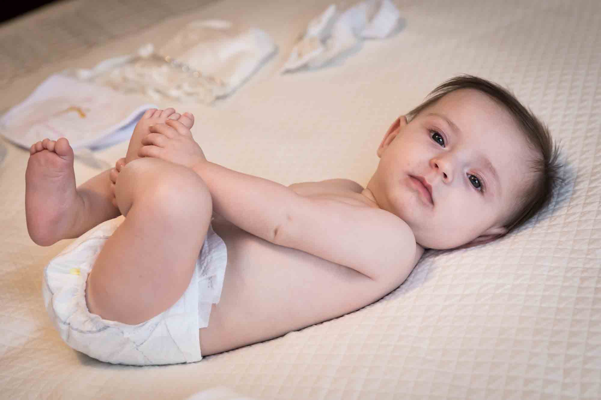 Naked baby wearing diaper on white bedspread