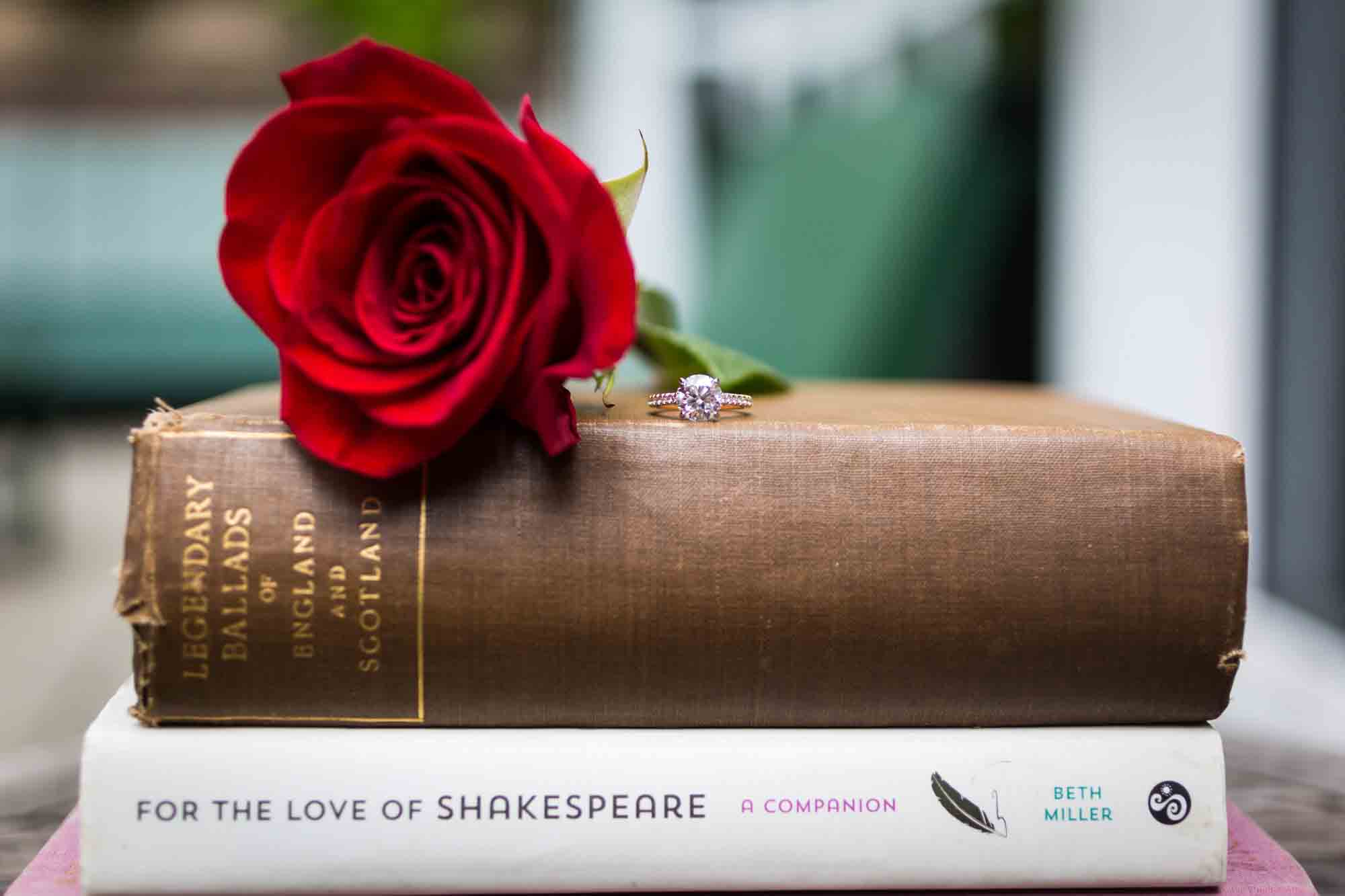 Engagement ring on top of books with red rose flower