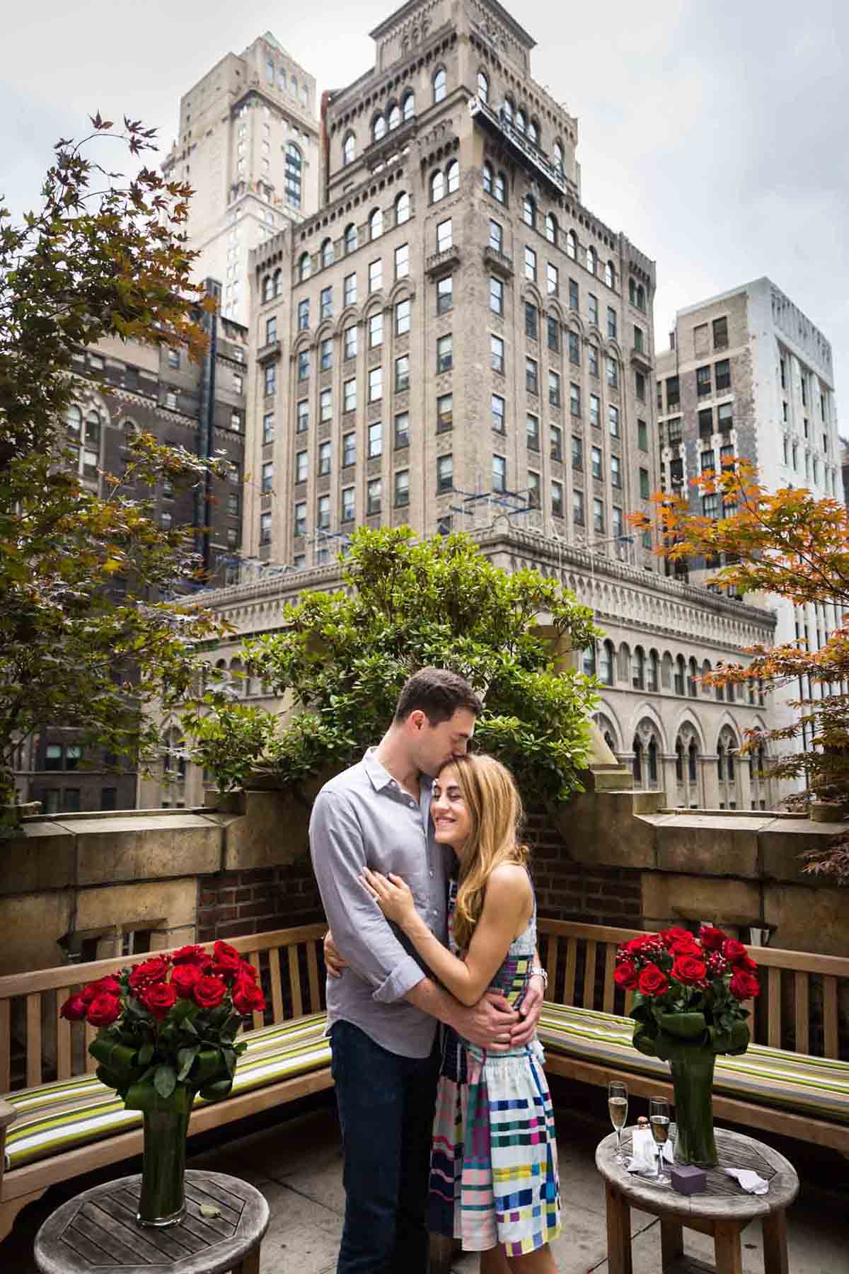 Couple hugging on the patio of the Library Hotel with building in the background after proposal