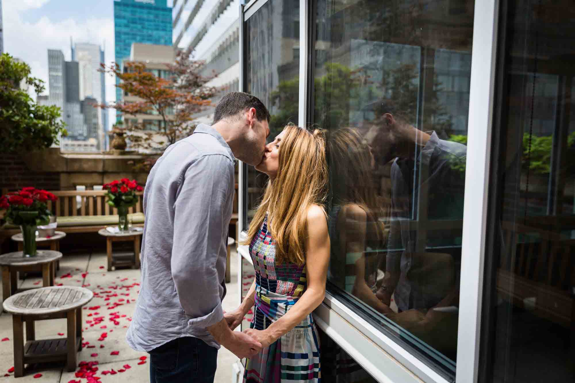 Couple kissing against window with reflection after proposal at the Library Hotel