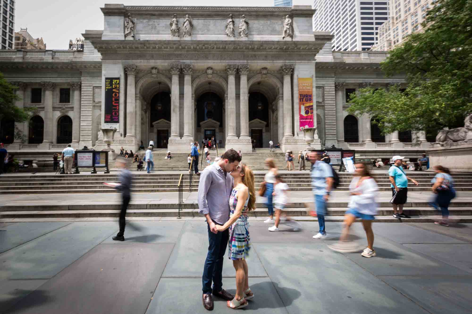 Couple kissing in front of library with blur of other people passing by during a New York public library engagement photo shoot