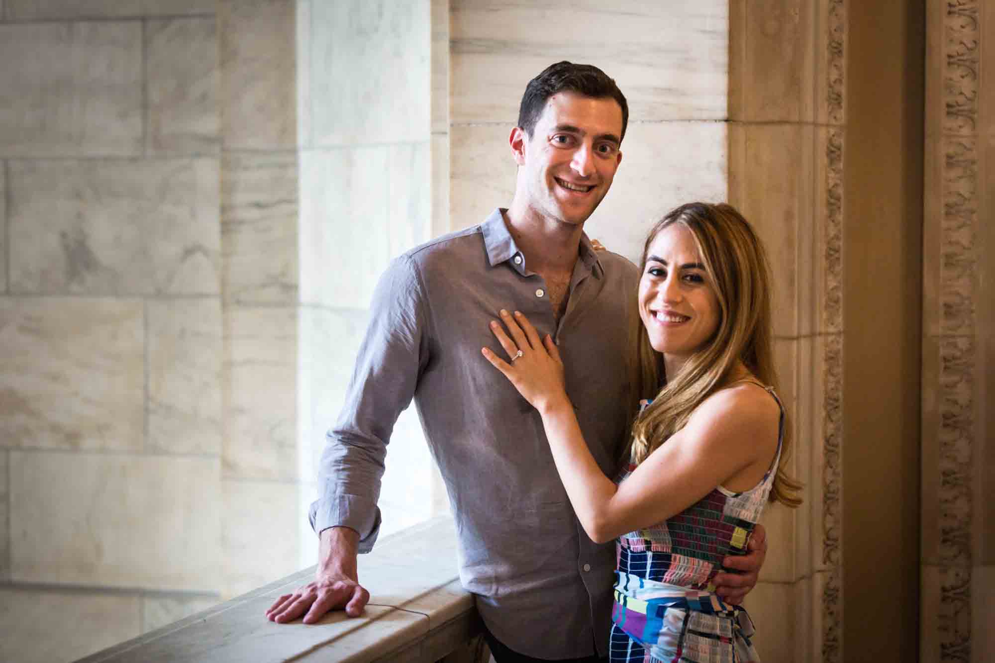Couple hugging in front of a marble wall during a New York public library engagement photo shoot