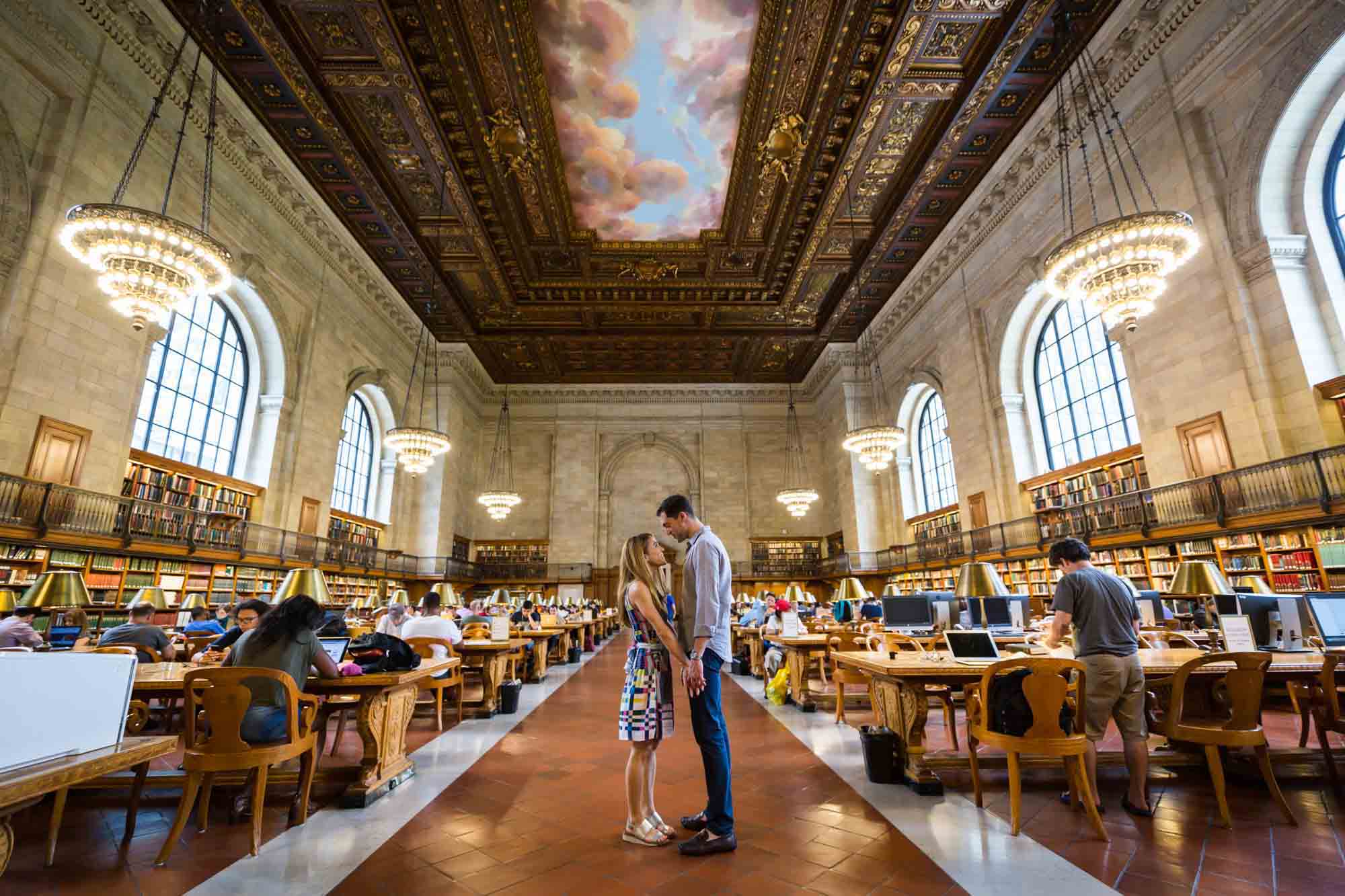 Couple holding hands in the Rose Main Reading Room during a New York public library engagement photo shoot