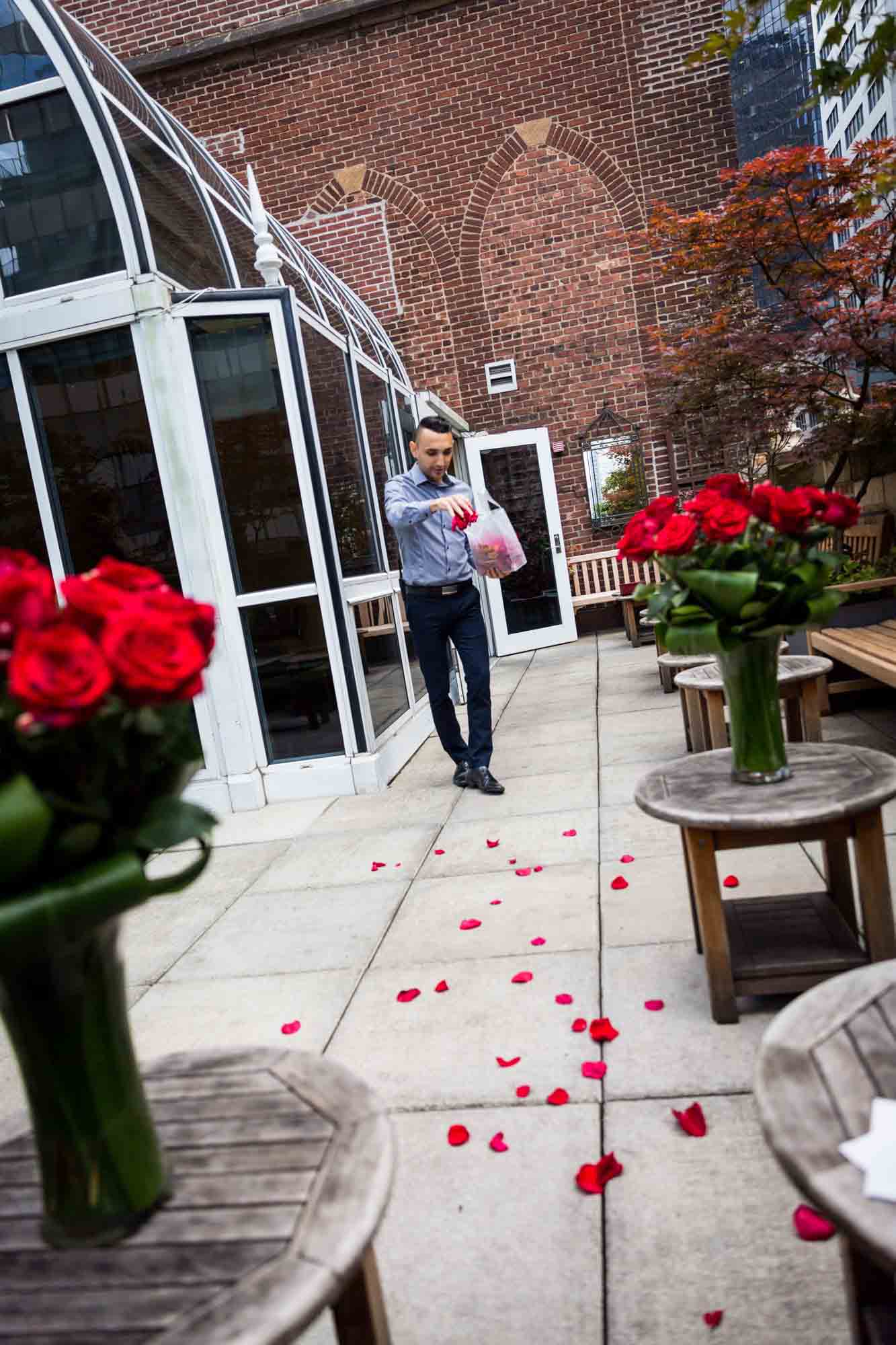 Man distributing red rose petals from a bag on a patio at the Library Hotel