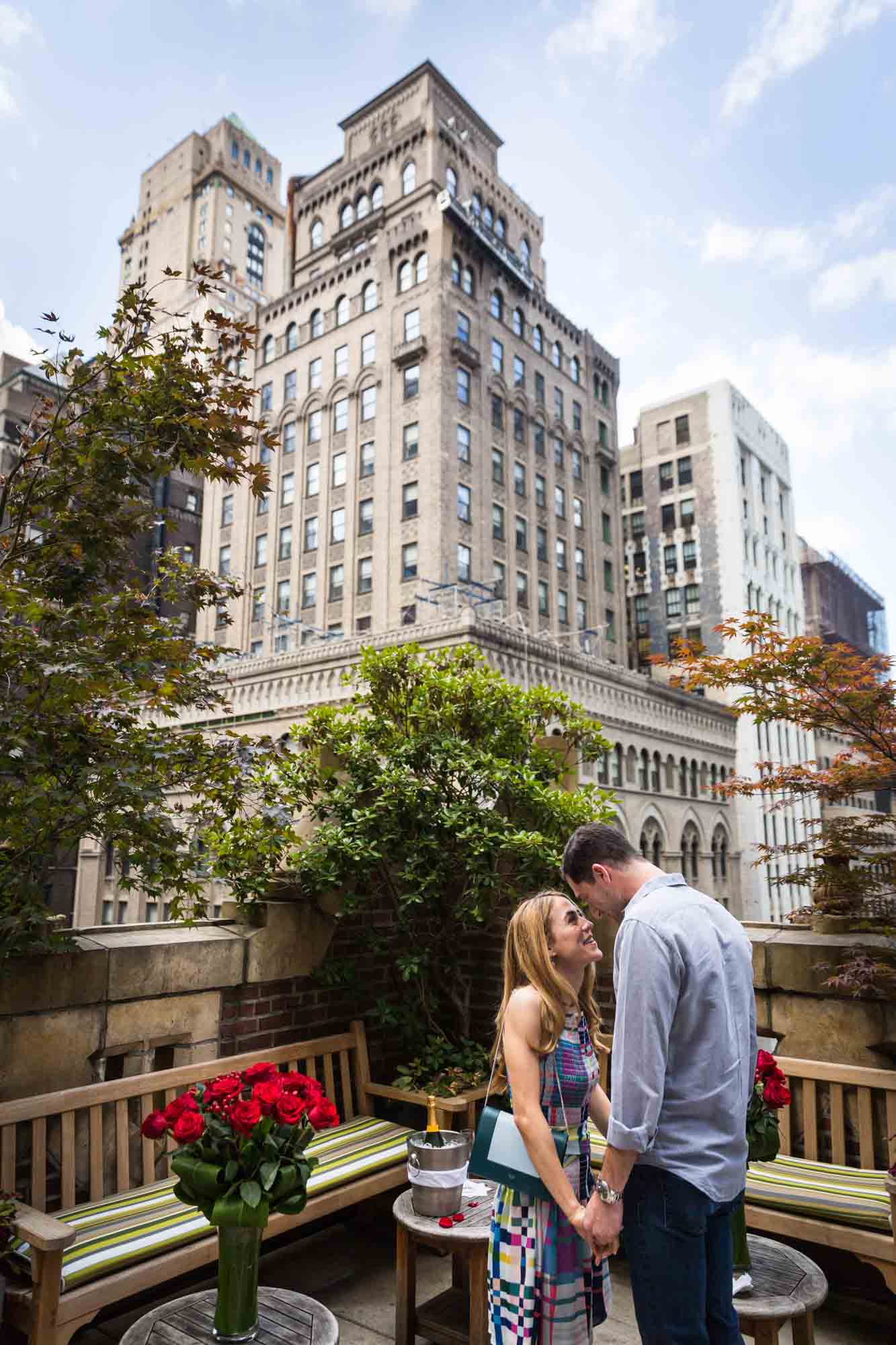 Couple hugging on the patio of the Library Hotel with building in the background after proposal