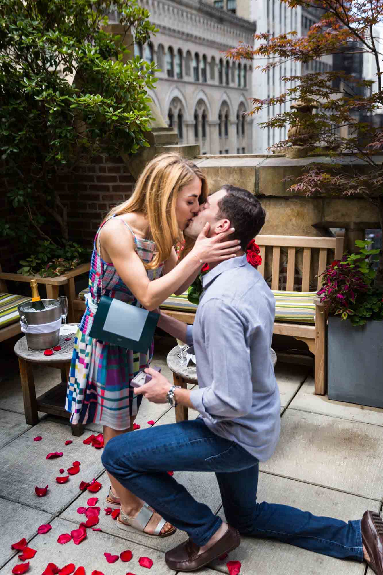 Woman kissing man sitting on one knee after proposing at the Library Hotel