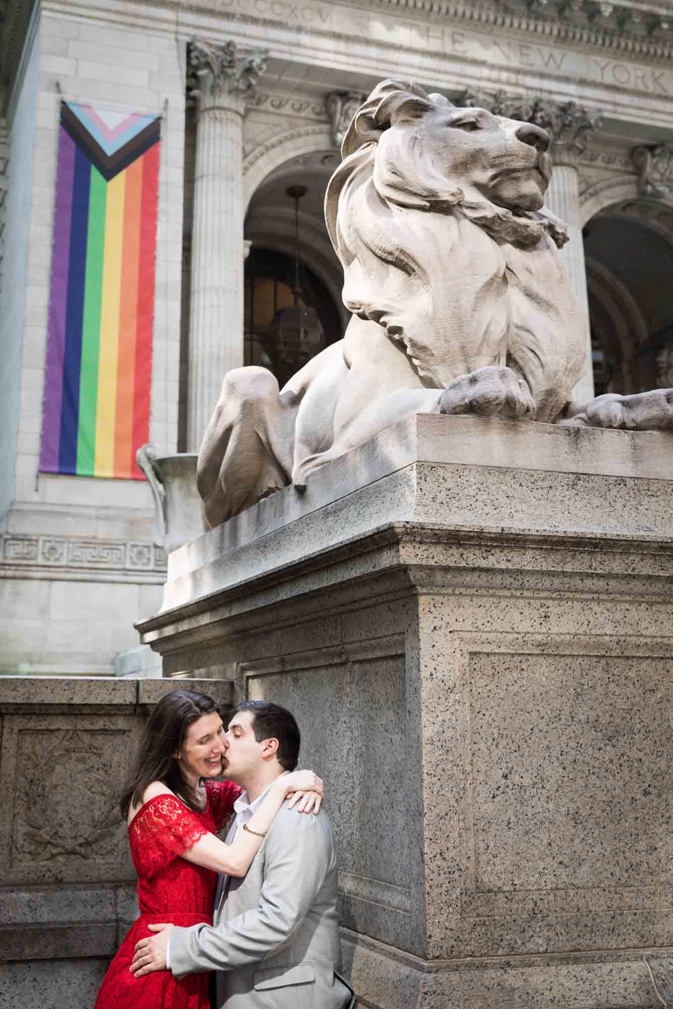 Man in grey jacket kissing woman in red dress below stone lions at New York Public Library proposal