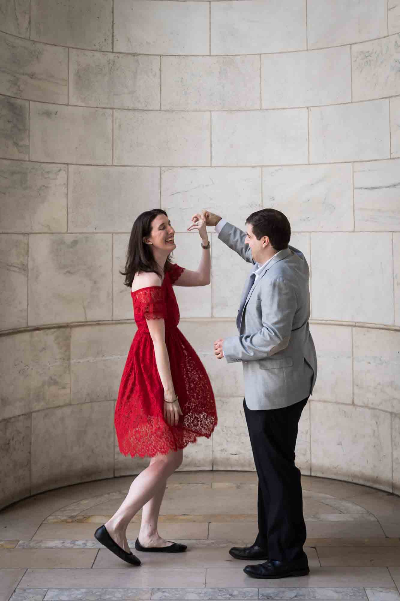 Man dancing with woman wearing red dress in marble alcove Couple hugging in marble alcove with woman wearing red dress during a New York Public Library surprise proposal