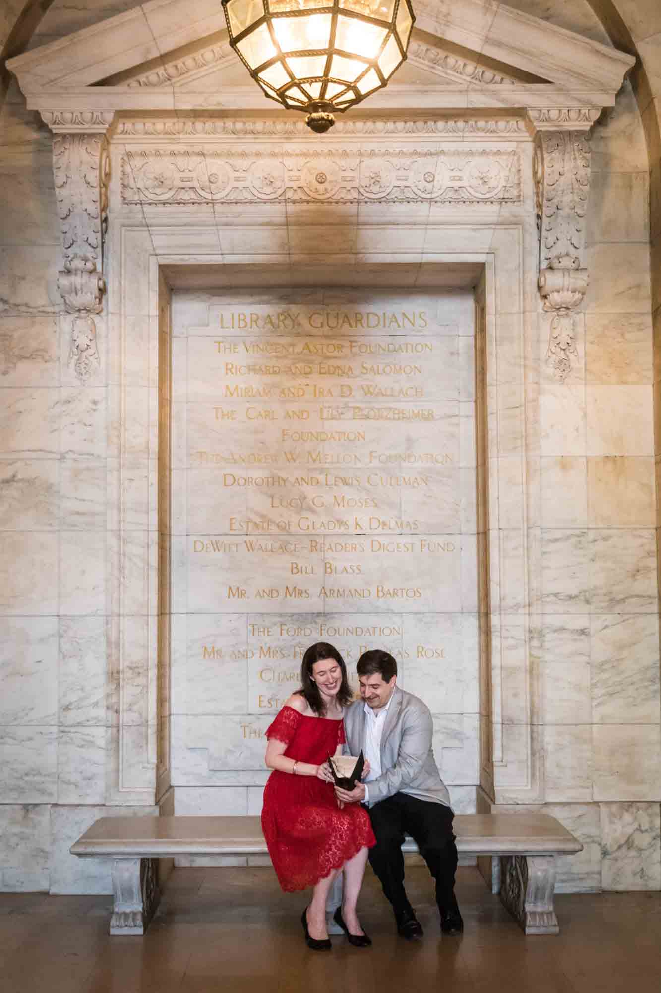 Couple reading book while sitting on stone bench under stone door frame during a New York Public Library surprise proposal