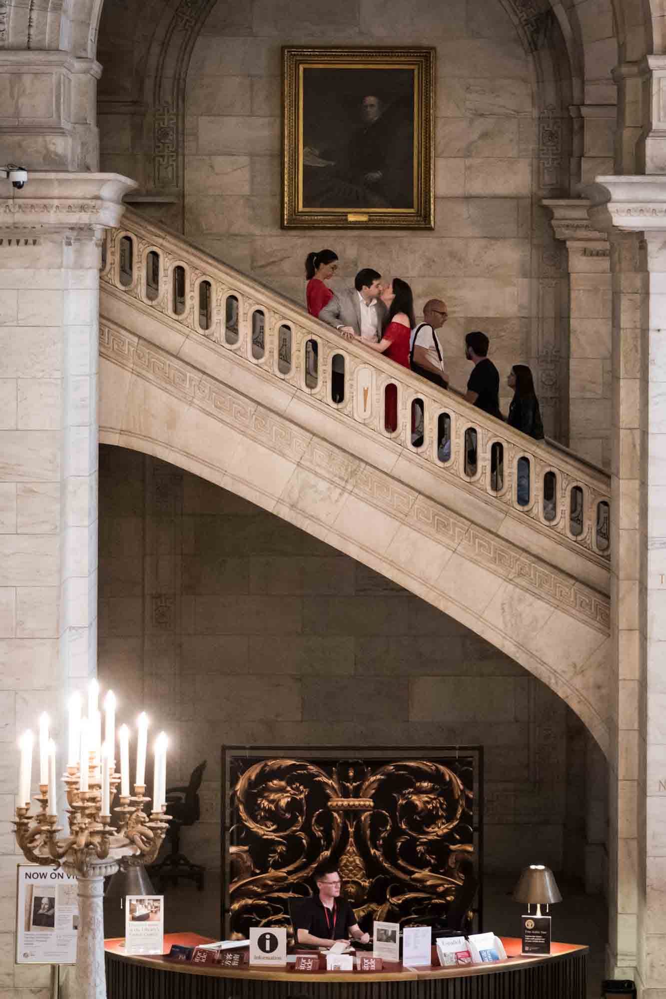 Couple kissing on second floor of main staircase with librarian below at desk during a New York Public Library surprise proposal