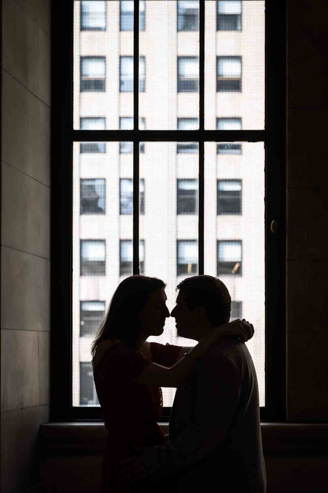 Backlit photo of couple about to kiss in front of a window during a New York Public Library proposal