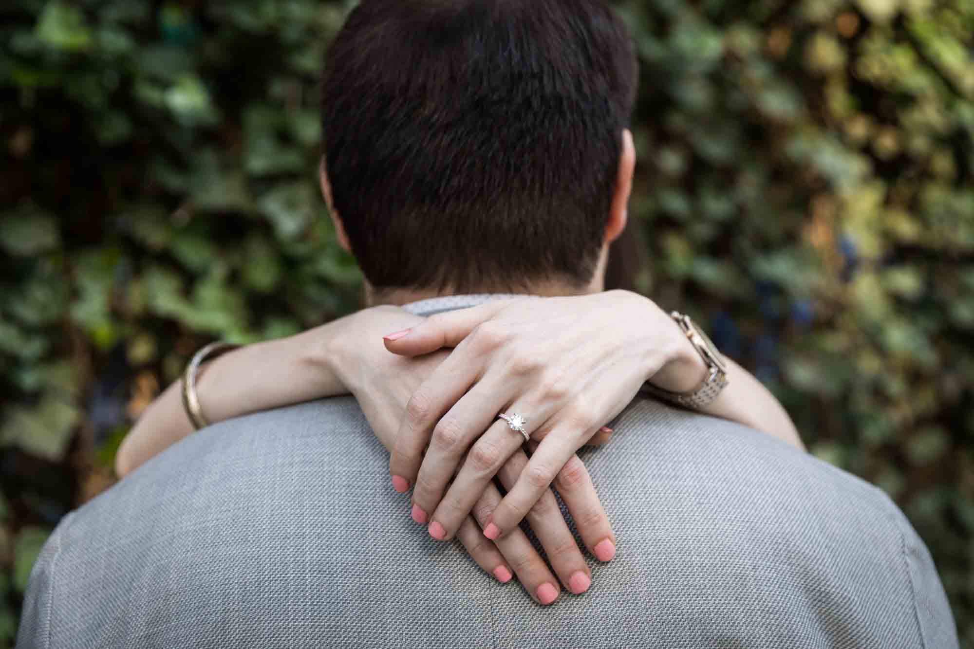 Close up of woman's hands wearing engagement ring around man's neck in garden