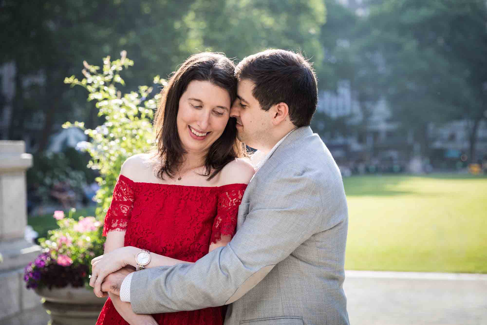 Man in grey jacket hugging woman in red dress in Bryant Park