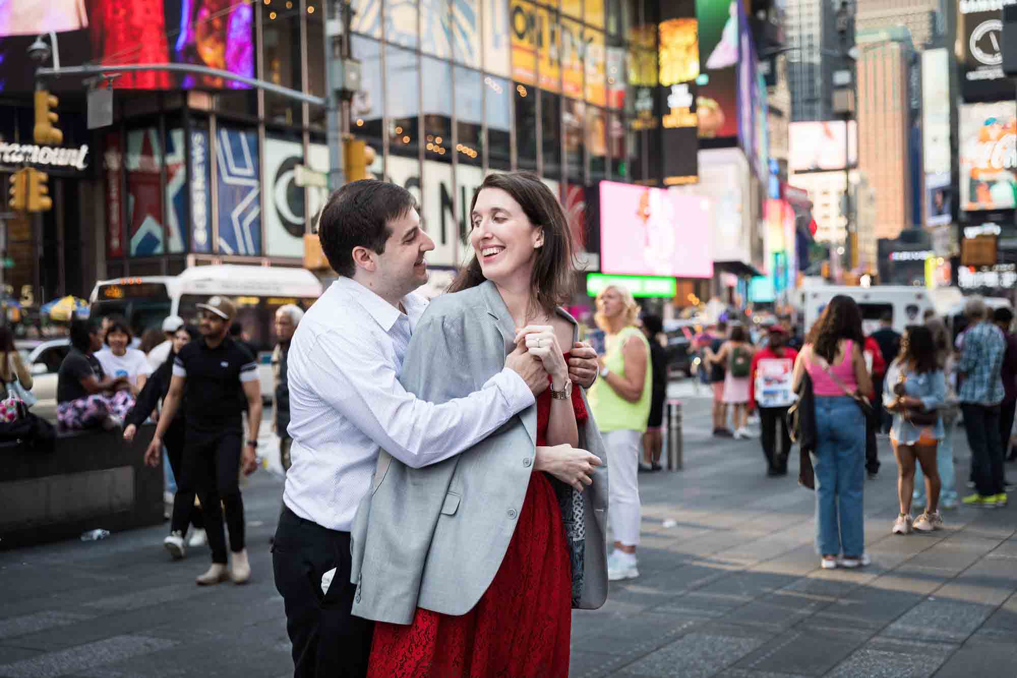 Man putting grey jacket over woman's shoulders in Times Square