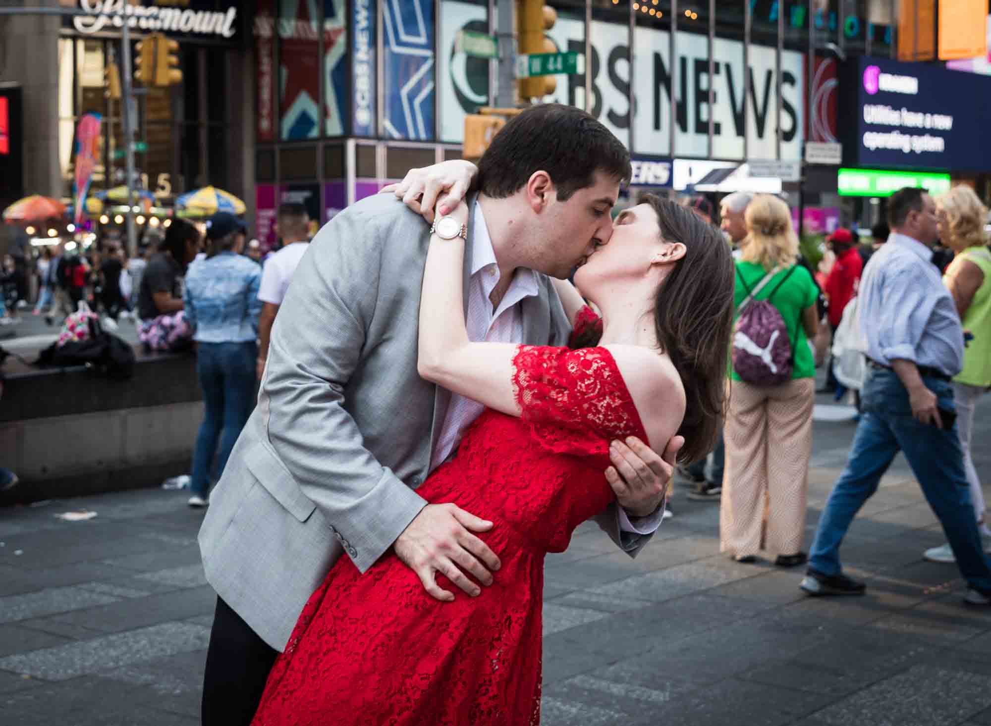 Woman in red dress kissing man in grey jacket in Times Square