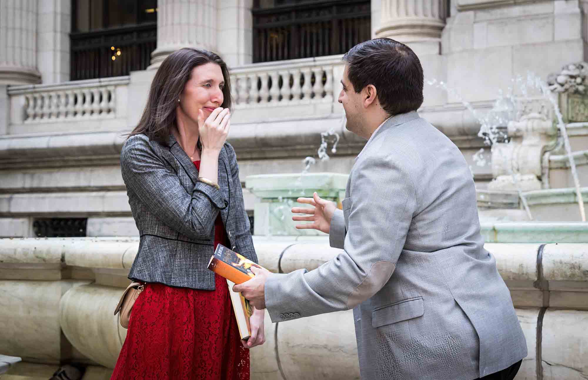Woman in red dress about to cry in front of man wearing grey jacket during New York Public Library proposal