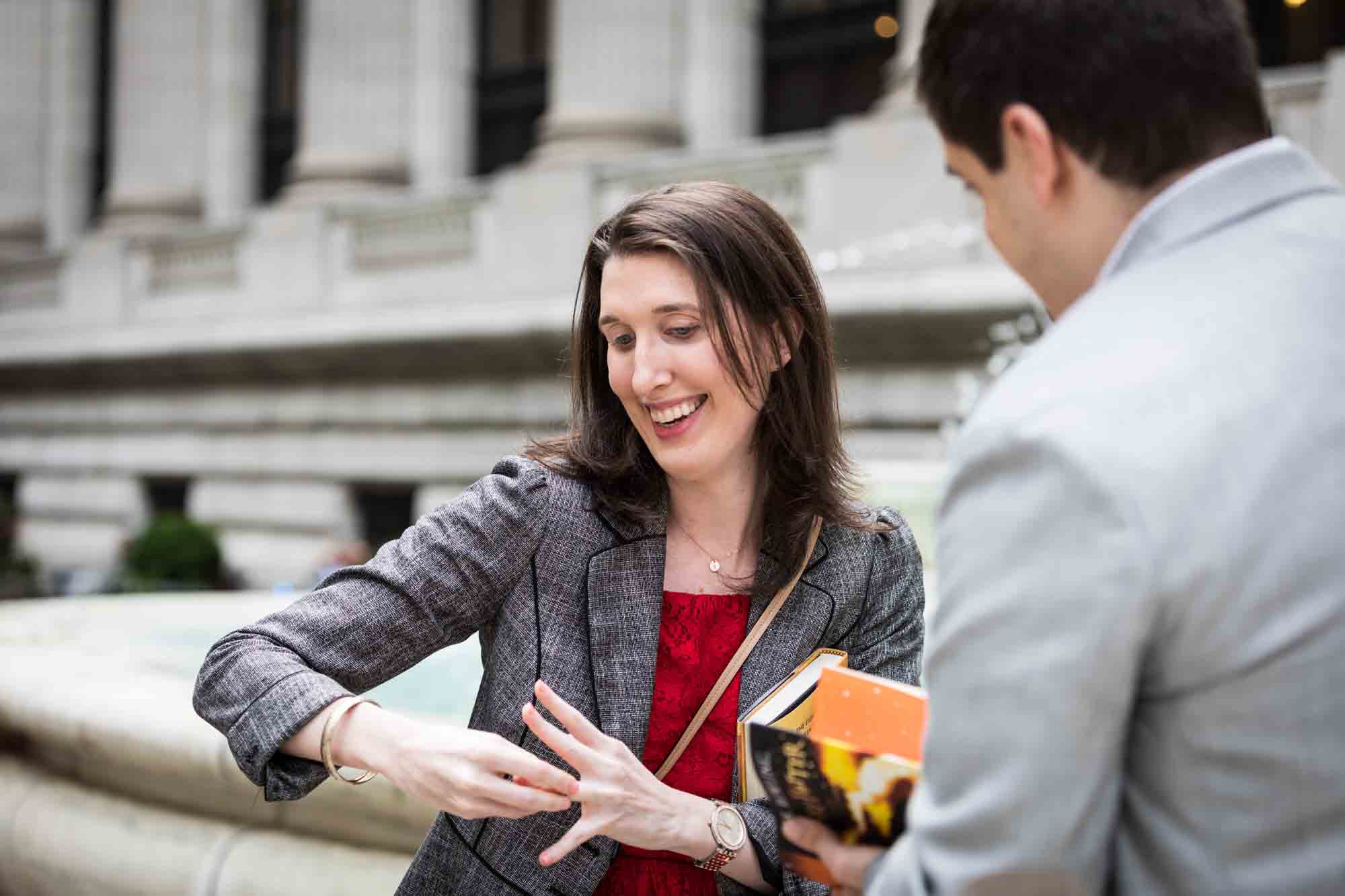 Woman wearing grey jacket trying to put on engagement ring after New York Public Library proposal