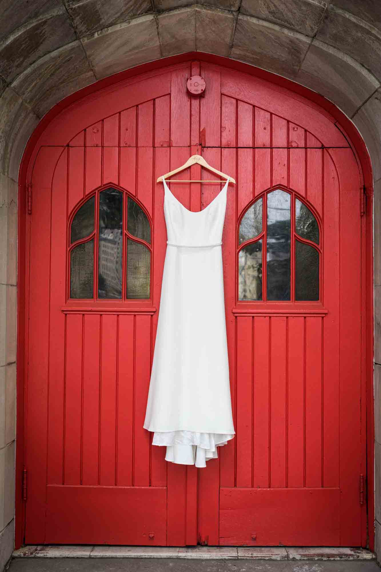 White wedding dress hanging on hanger on red doors at a Sanctuary Roosevelt Island wedding