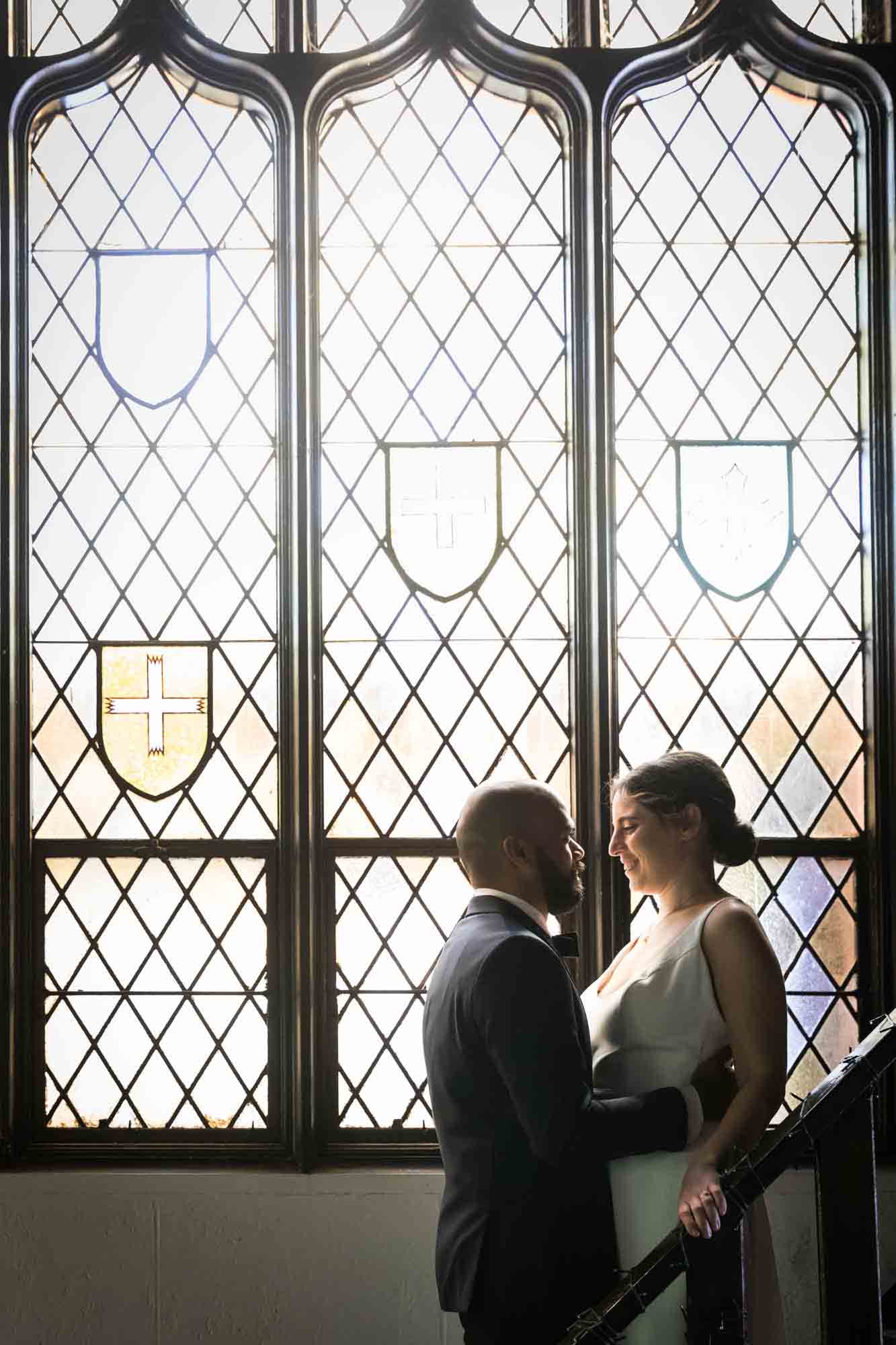 Bride and groom looking at each other on stairs in front of stained glass window at a Sanctuary Roosevelt Island wedding