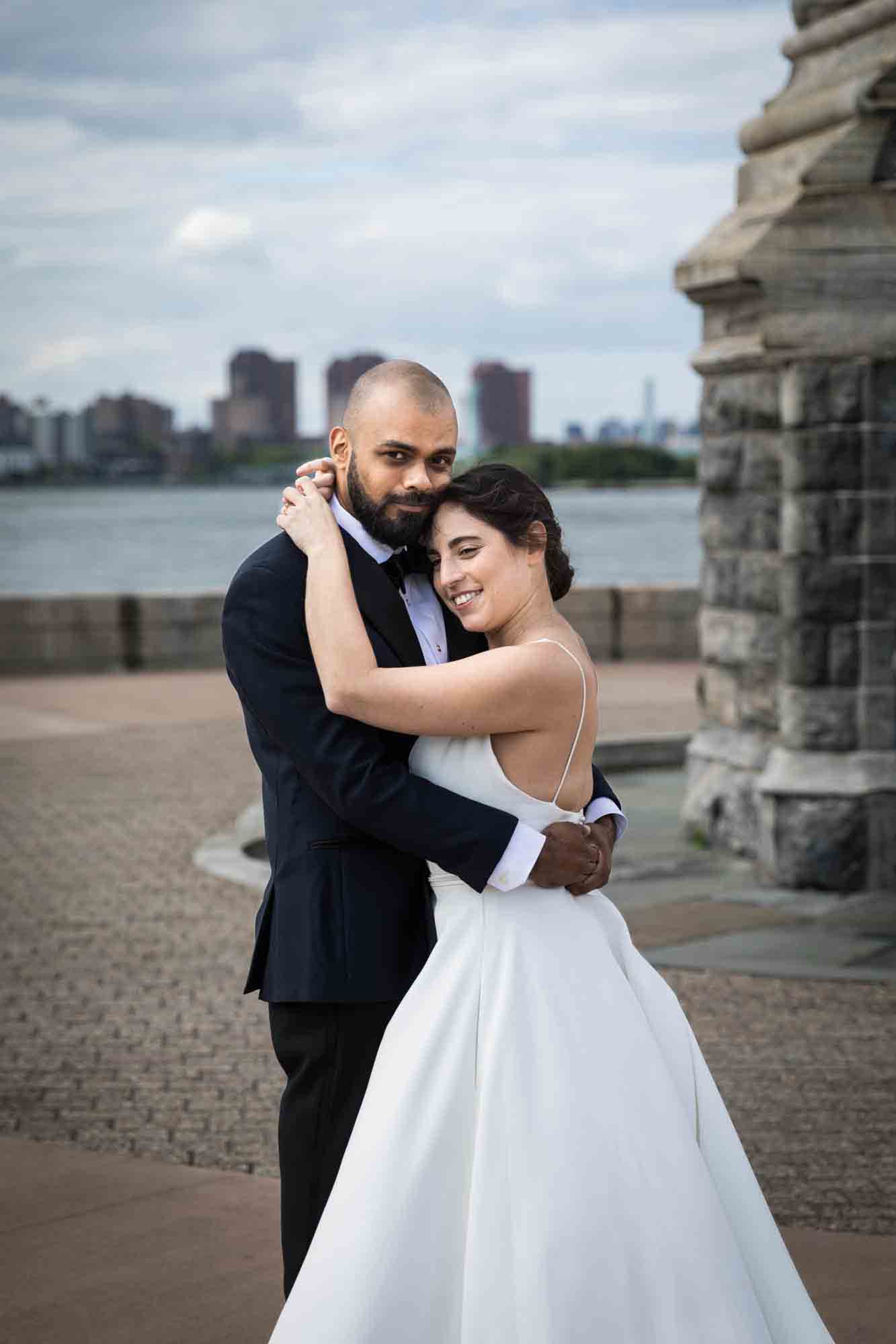 Bride and groom hugging in front of lighthouse in front of NYC skyline on Roosevelt Island