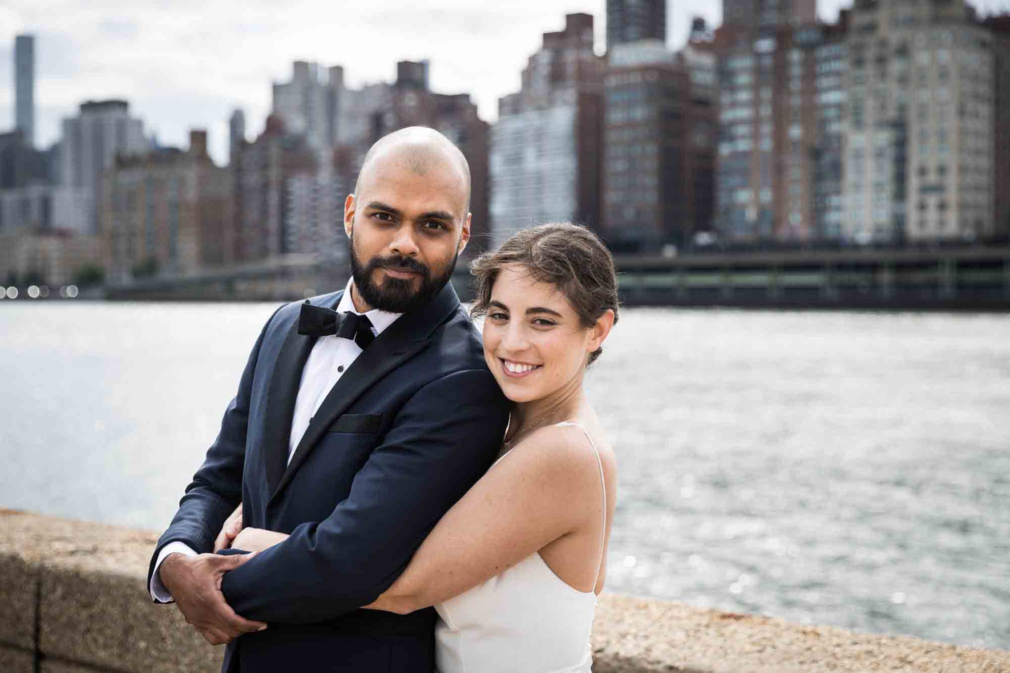 Bride hugging groom from behind in front of NYC skyline on Roosevelt Island