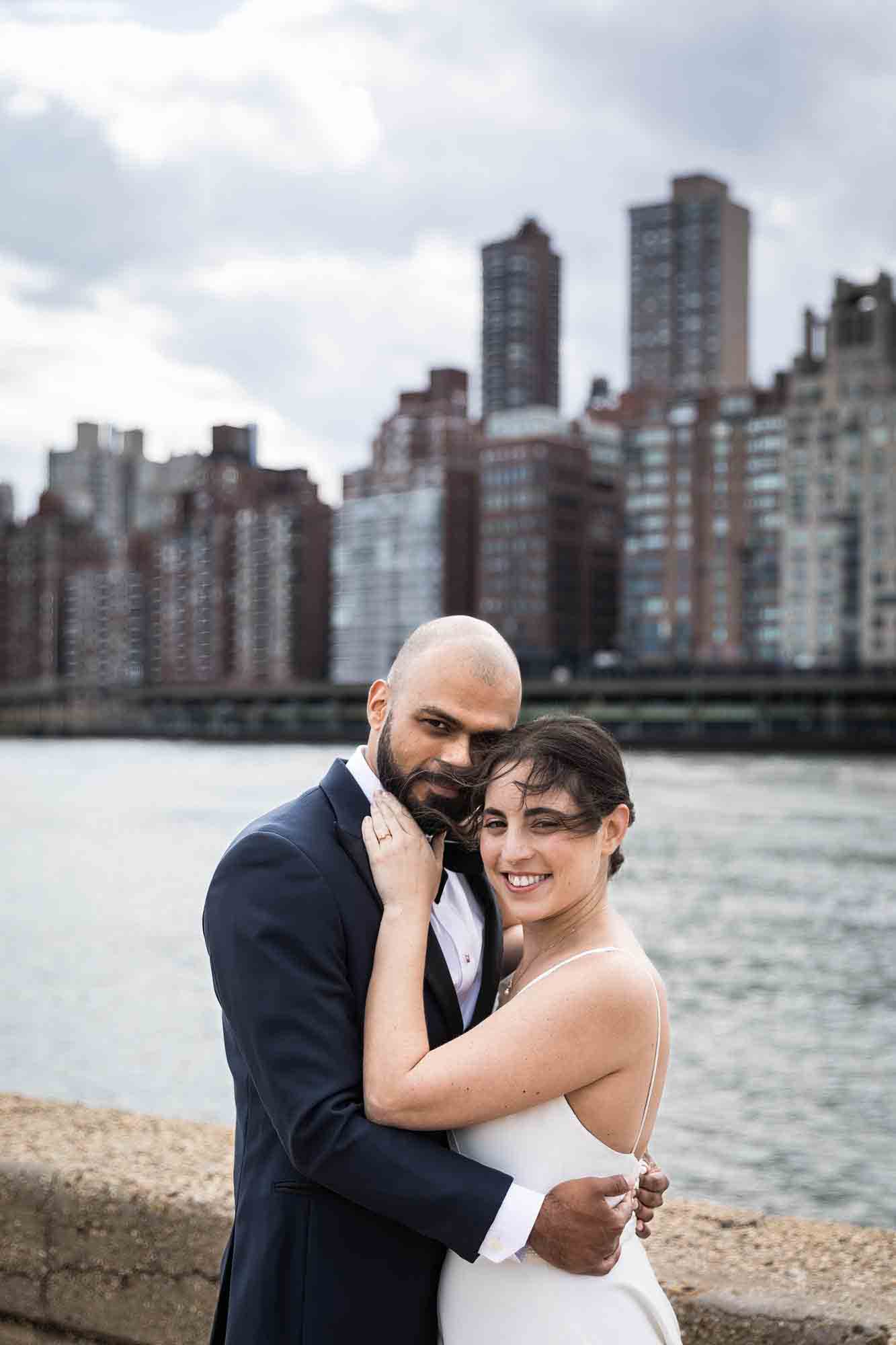 Bride and groom hugging in front of NYC skyline on Roosevelt Island